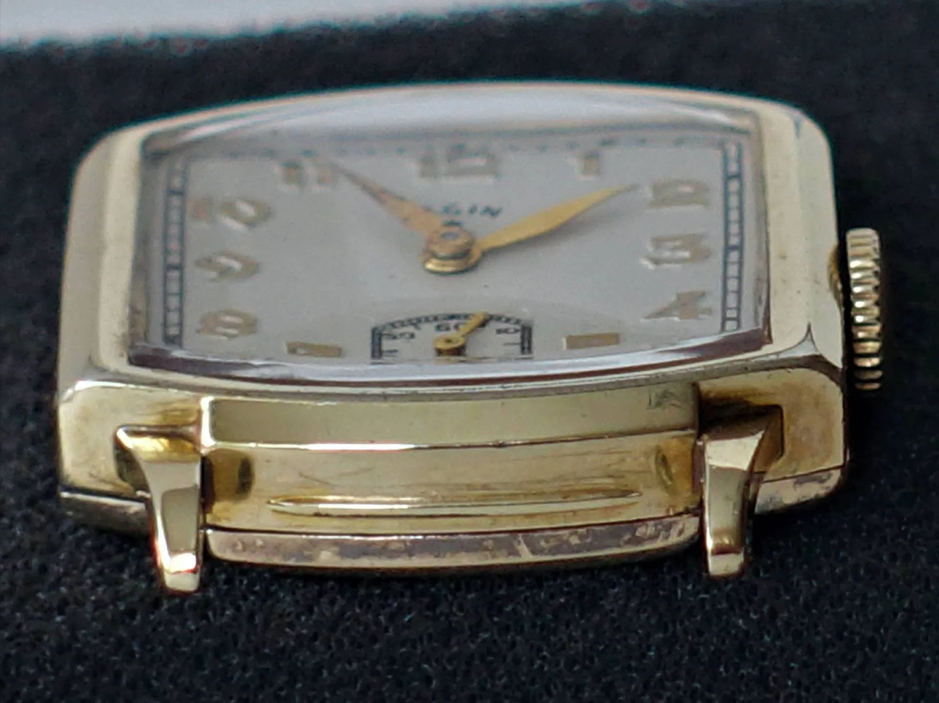 Rechteckige gelbgoldfarbene Vintage-Uhr Eine rechteckige Armbanduhr mit gelbgoldfarbenem Gehäuse, weißen Zifferblatt und goldfarbenen Zeigern, aus der Nähe fotografiert.