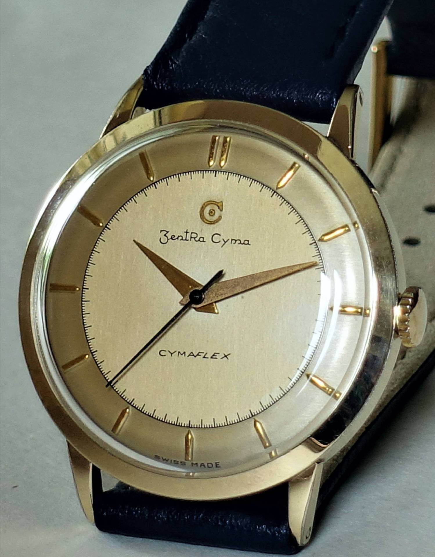 Goldfarbene Armbanduhr mit hellem Zifferblatt und schwarzem Armband.