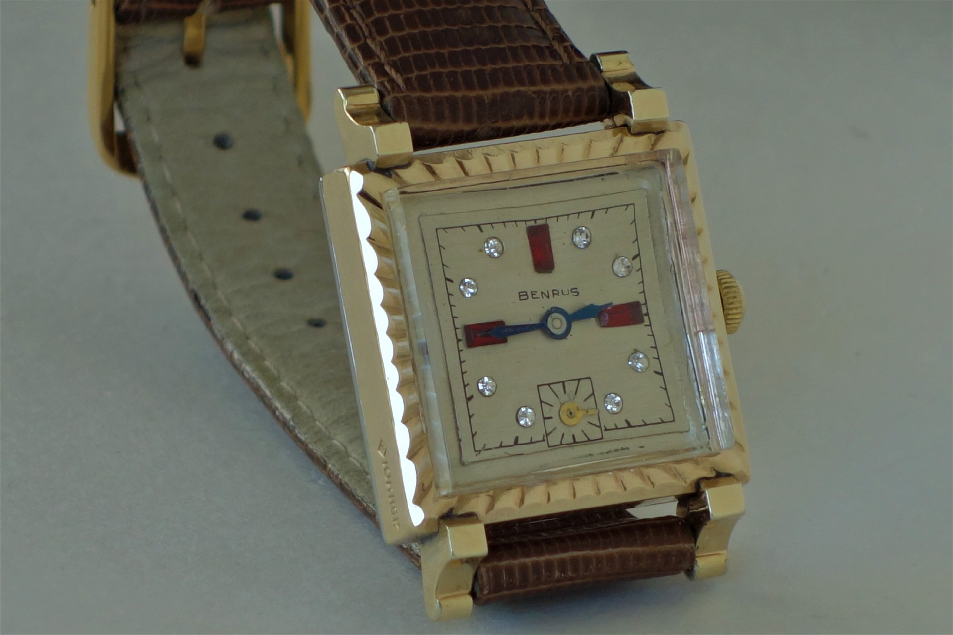 Eckige Armbanduhr von Benrus mit goldfarbenem Gehäuse, hellen Zifferblatt und braunem Lederarmband.
