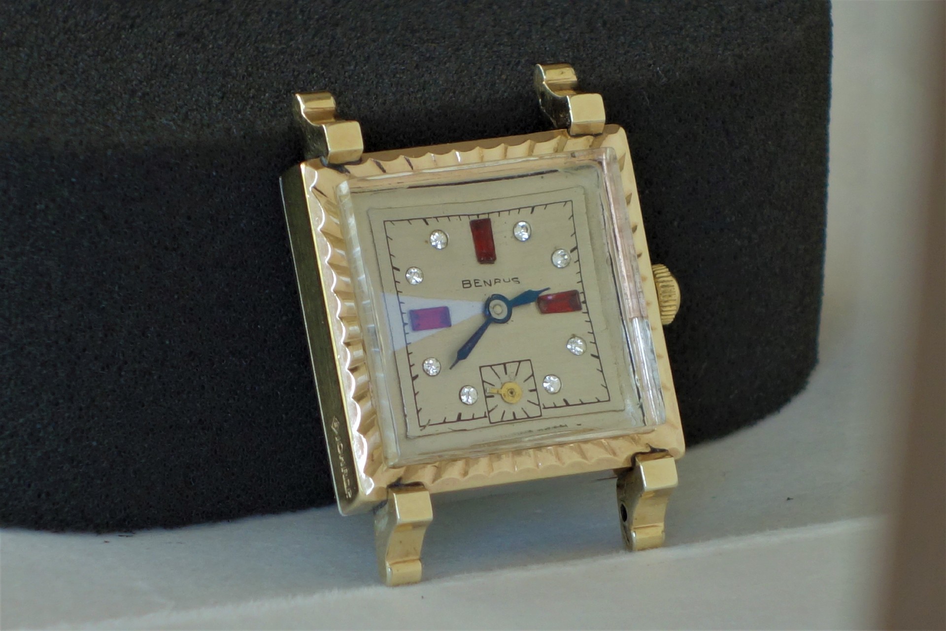 Rechteckige Armbanduhr mit hellem Zifferblatt, Metallgehäuse und Schmucksteinen als Indizes.