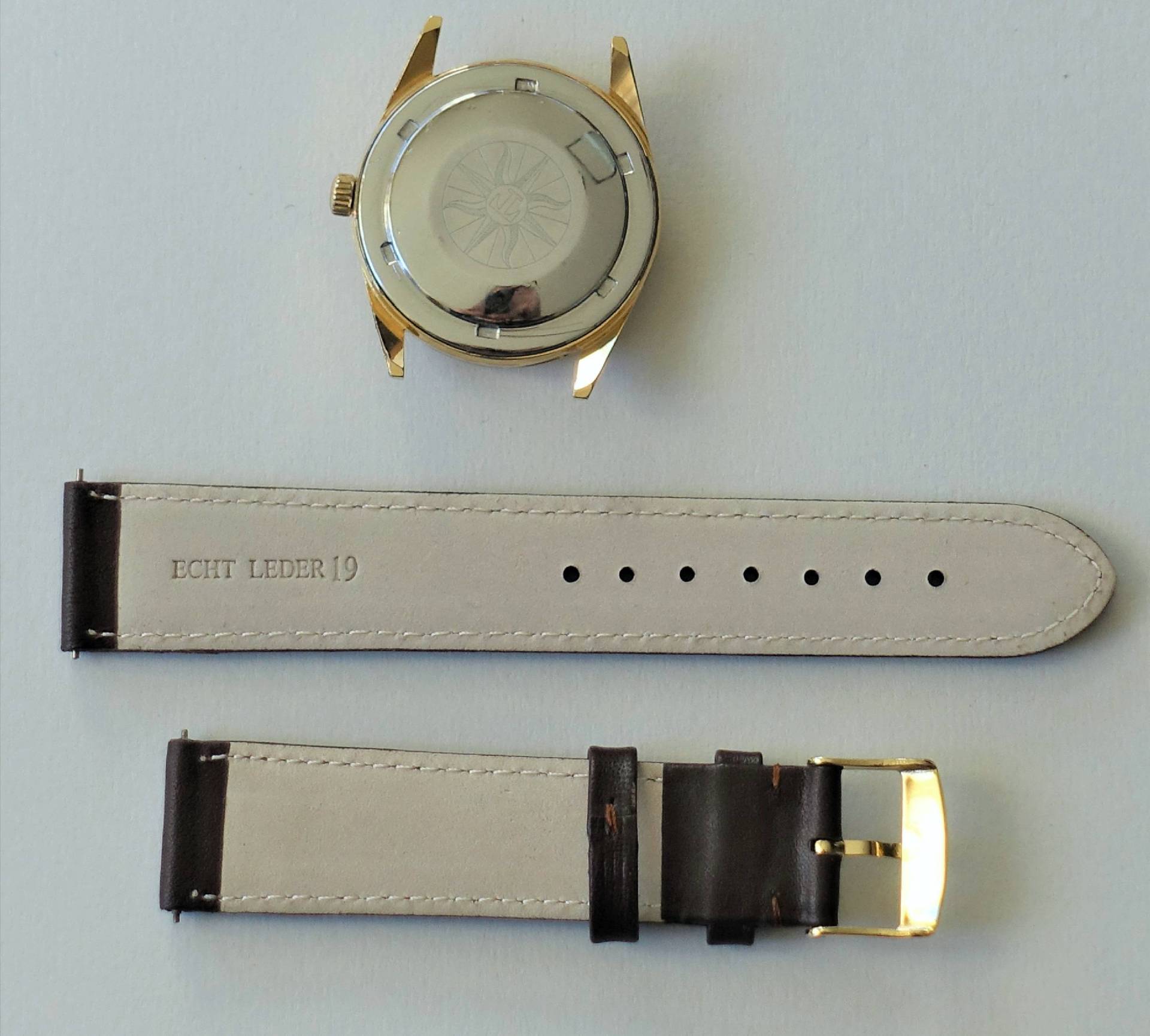 Goldfarbenes Uhrgehäuse mit silberner Rückseite und dunkelbraunes Lederarmband mit goldfarbener Schließe.