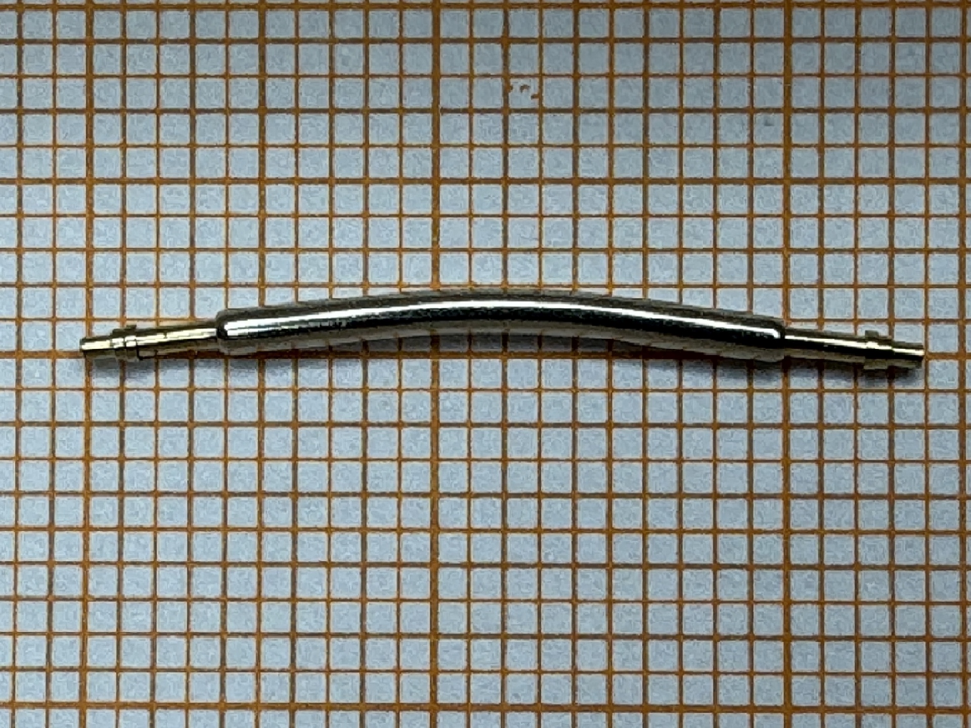 Gebogener Federsteg aus Metall für Uhrenarmbänder auf kariertem Hintergrund.