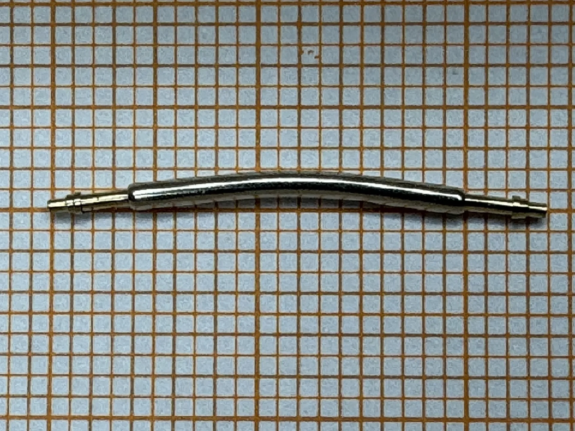 Gebogener Federsteg Metall Gebogener Federsteg aus Metall für Uhrenarmbänder auf kariertem Hintergrund.