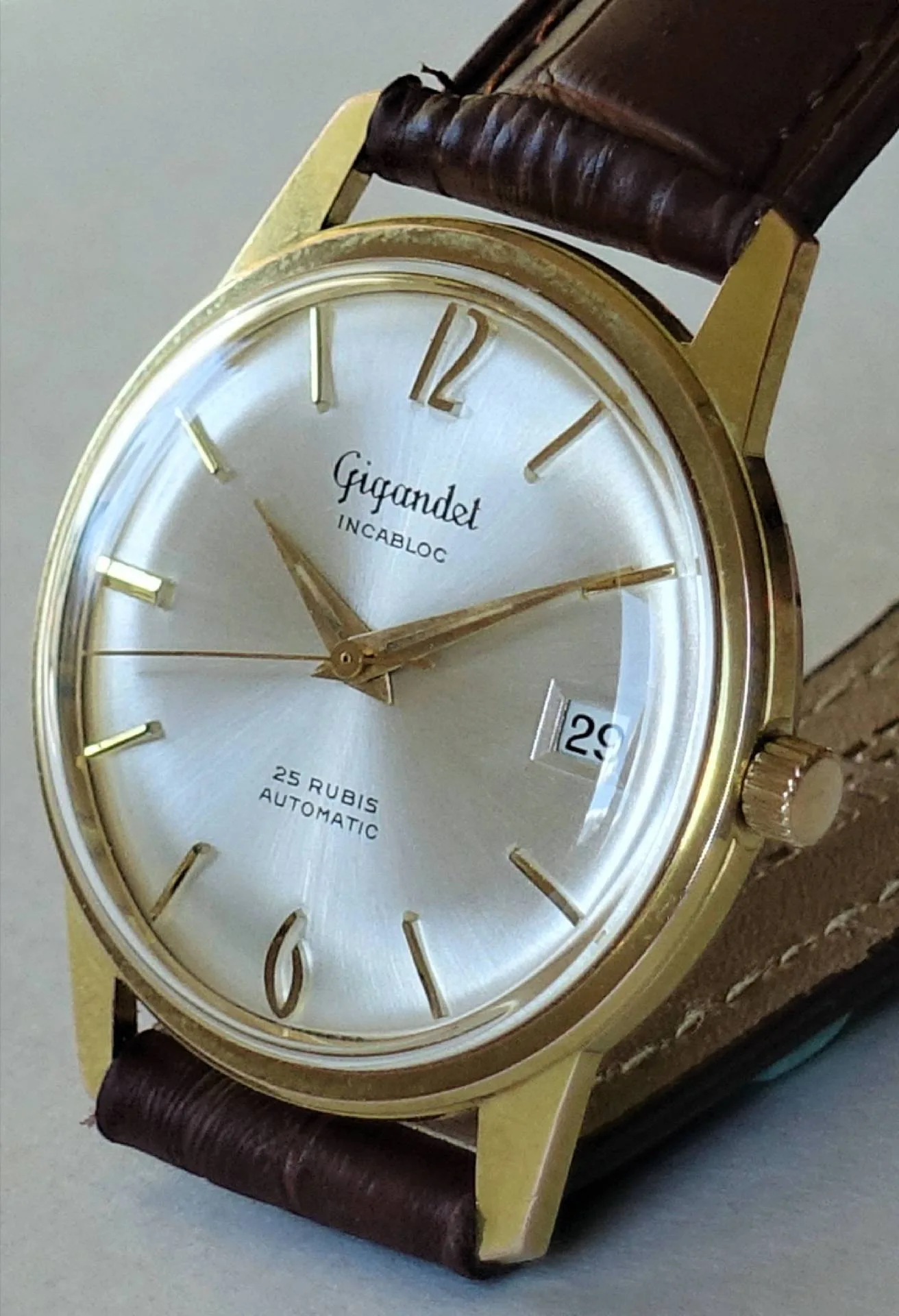 Goldfarben Silbernes Zifferblatt Braun Eine klassische Armbanduhr mit goldfarbenem Gehäuse, silbernem Zifferblatt, braunem Lederarmband und Datumsanzeige.