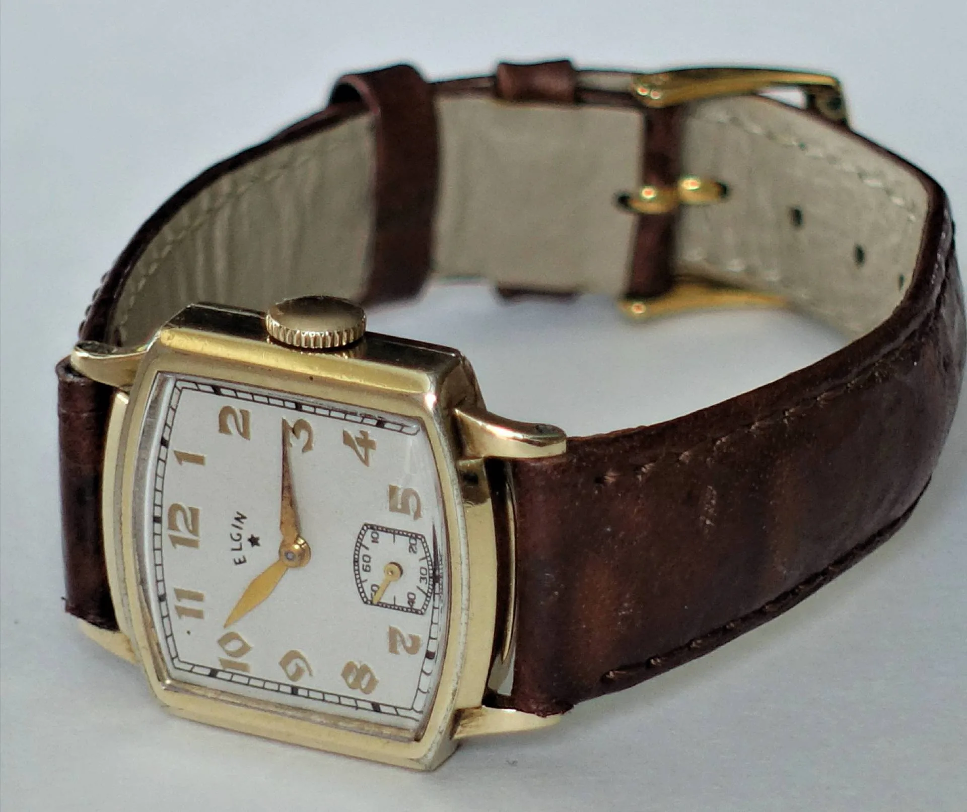 Rechteckige goldfarbene Vintage-Uhr Eine rechteckige, goldfarbene Armbanduhr mit weißem Zifferblatt, braunem Lederarmband und kleinen Sekundenanzeige bei sechs Uhr.