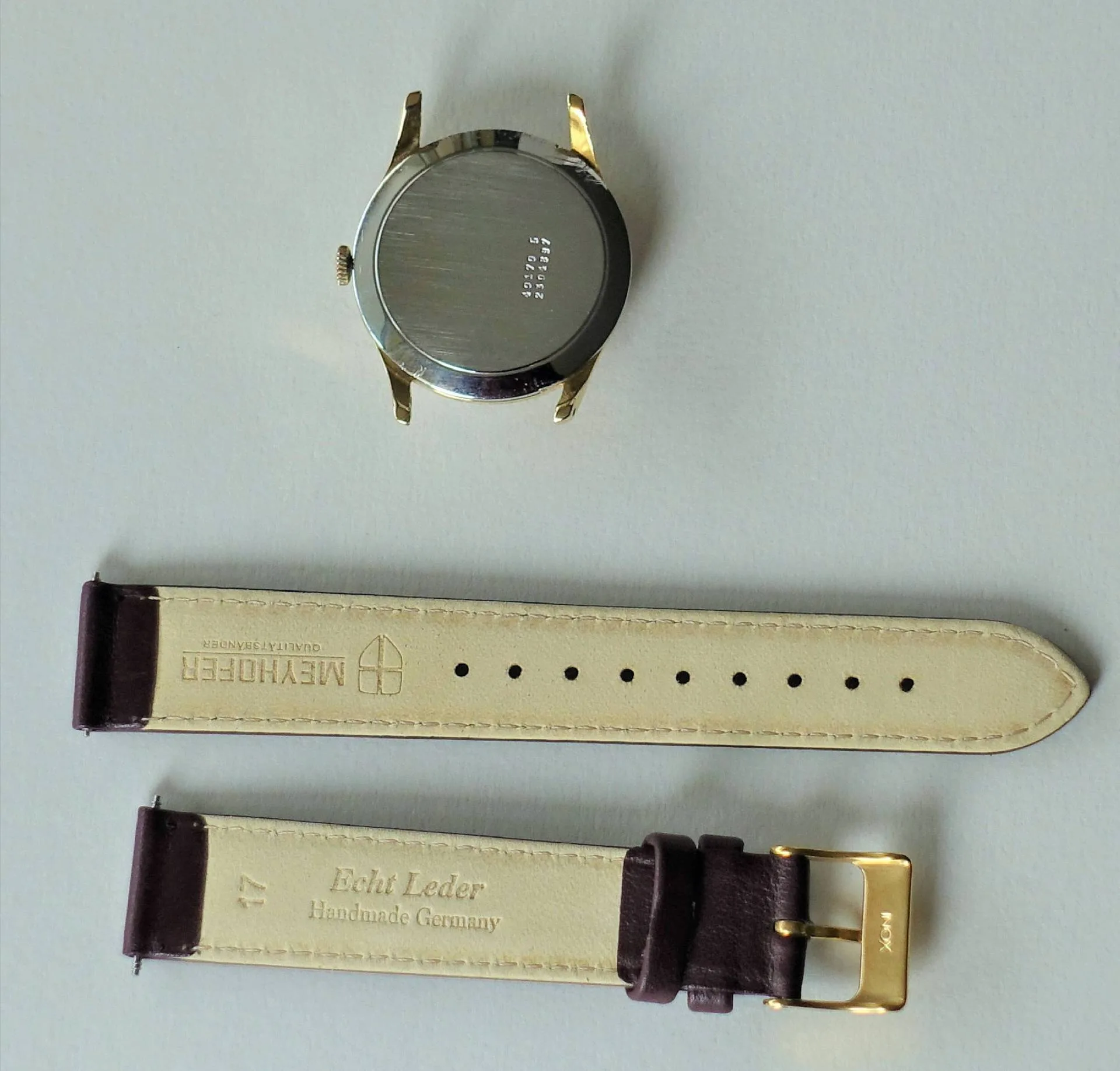 Uhrgehäuse goldfarben und Lederarmband Goldfarbenes Uhrgehäuse mit silberner Rückseite und dunkelbraunes Lederarmband mit goldfarbener Schließe.