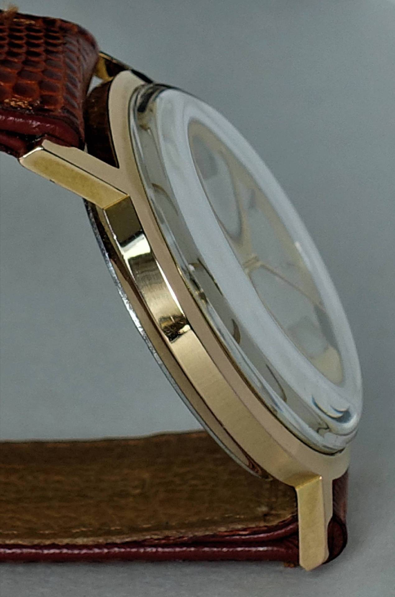 Flache Armbanduhr mit goldfarbenem Gehäuse und braunem Armband.