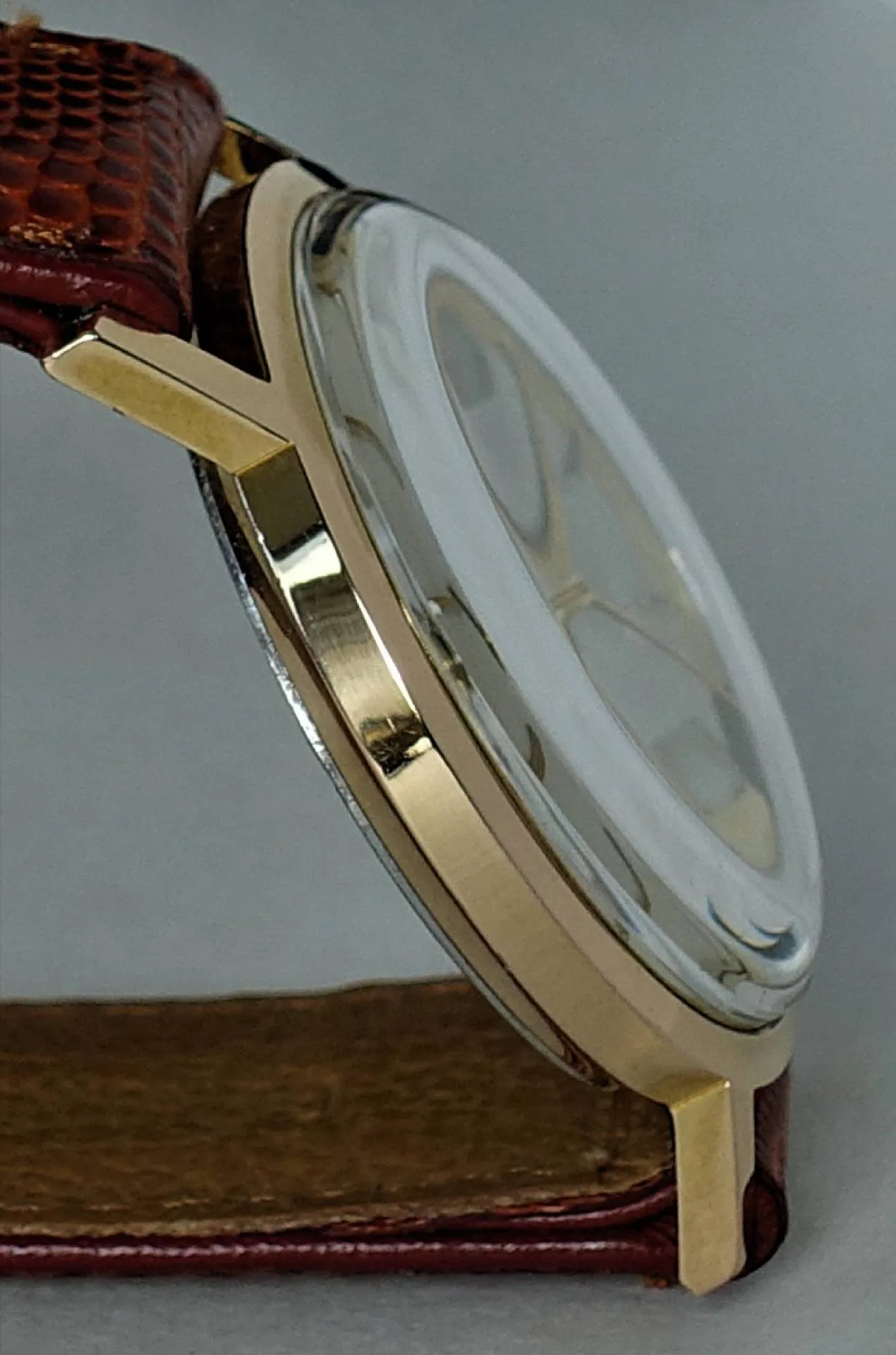 Flache Armbanduhr mit goldfarbenem Gehäuse und braunem Armband.
