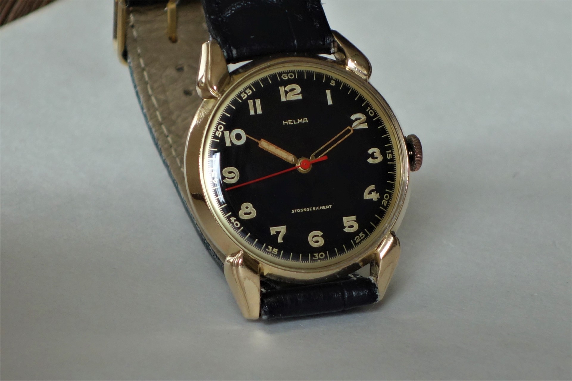 Analoge Armbanduhr mit schwarzem Zifferblatt, goldfarbenem Gehäuse und schwarzem Armband.