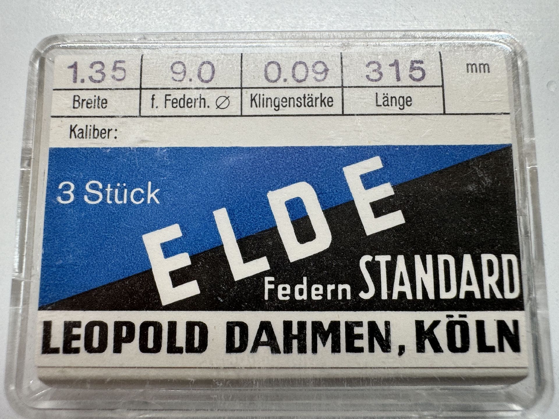 Verpackung mit drei Aufzugsfedern für Uhrwerke, beschriftet mit technischen Angaben.