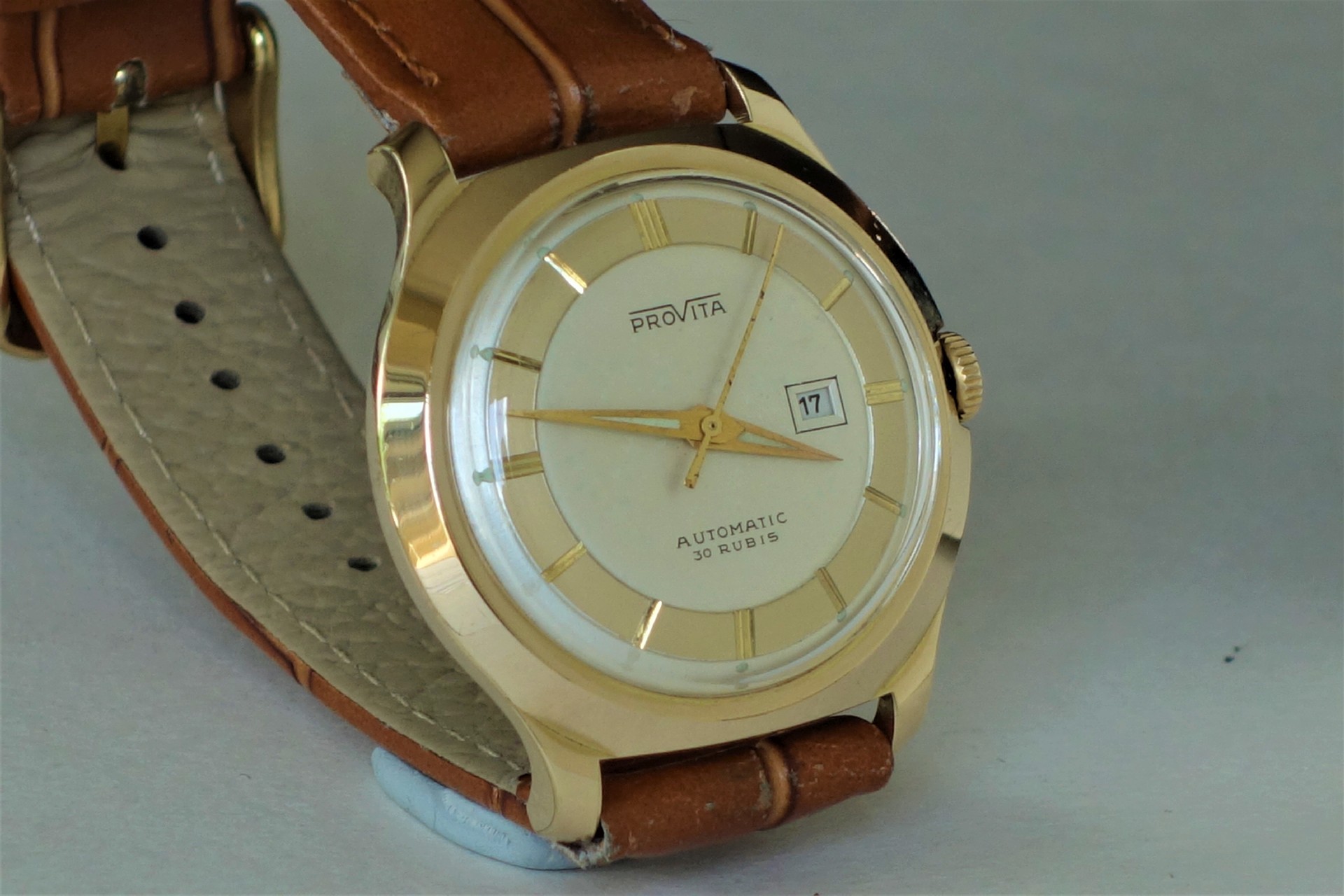 Goldfarbene Armbanduhr mit hellem Zifferblatt, Datumsanzeige und braunem Armband.