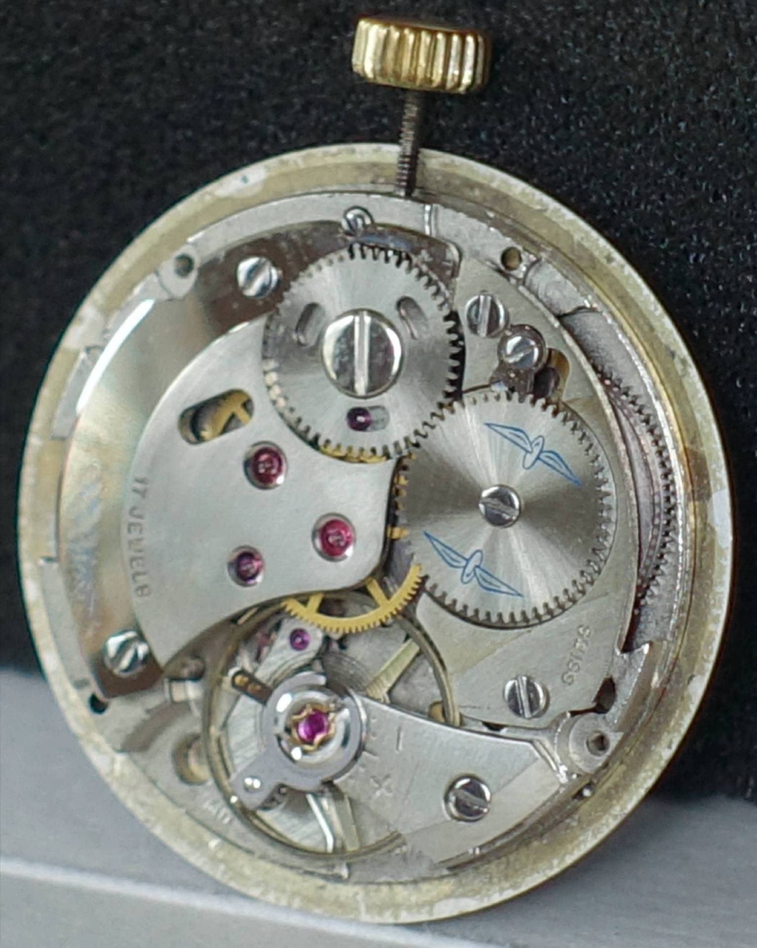 Silberfarbenes mechanisches Uhrwerk mit sichtbaren Zahnrädern und goldfarbener Krone.