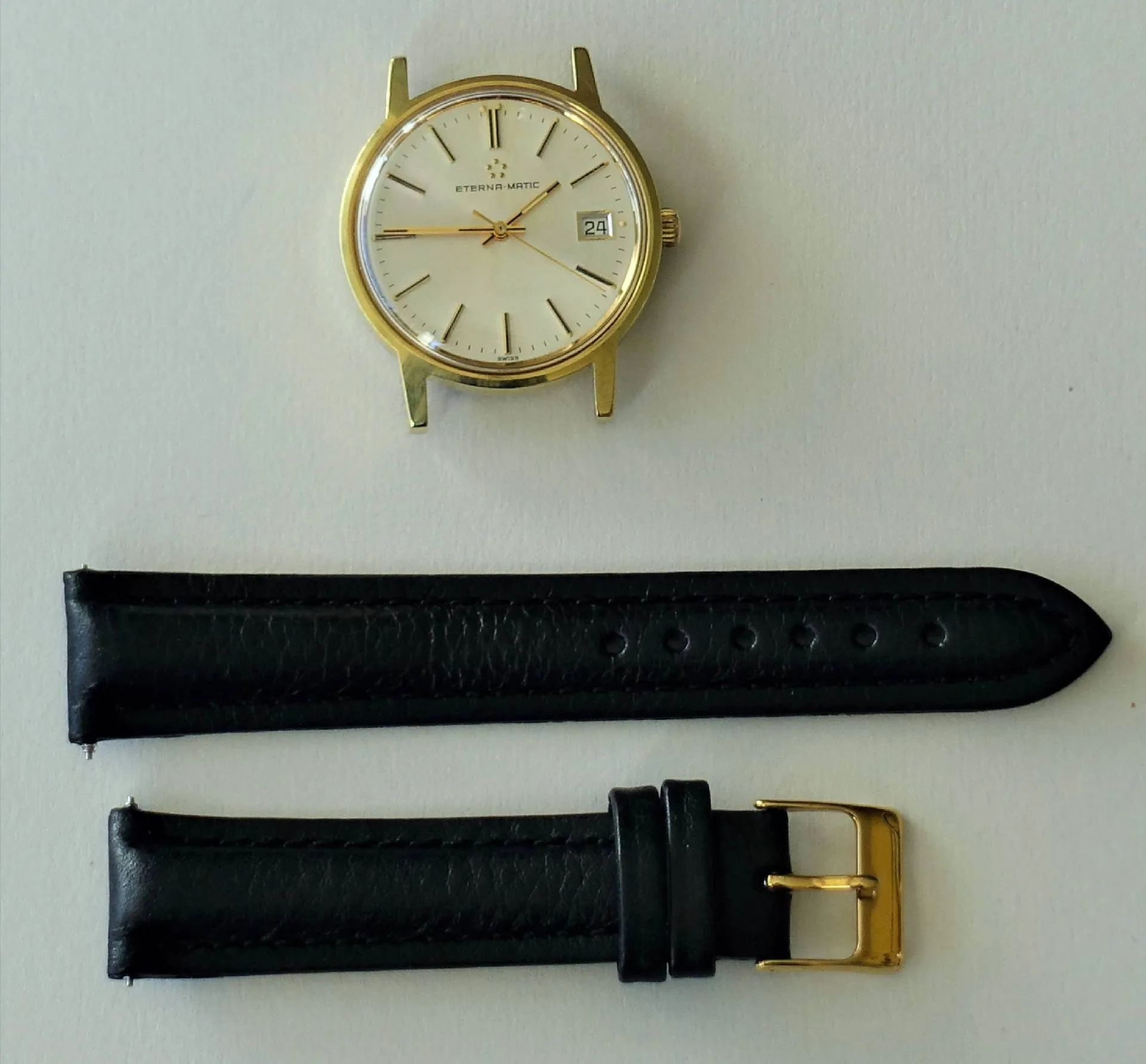 Goldfarbene Armbanduhr mit weißem Zifferblatt und schwarzem Lederarmband mit goldfarbener Schließe.