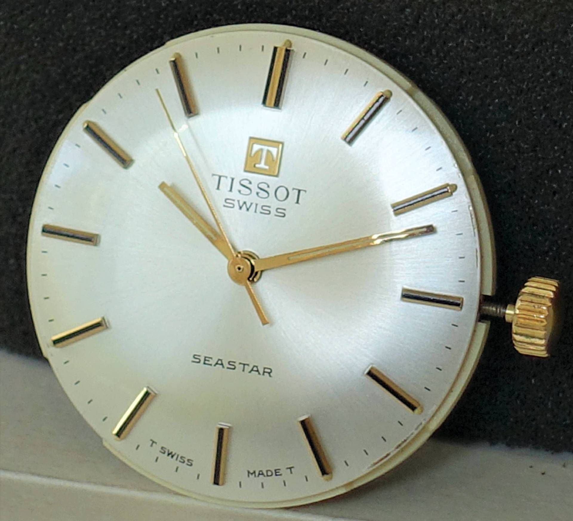 Silberfarbenes Zifferblatt mit goldfarbenen Zeigern und goldfarbener Krone für Armbanduhren.