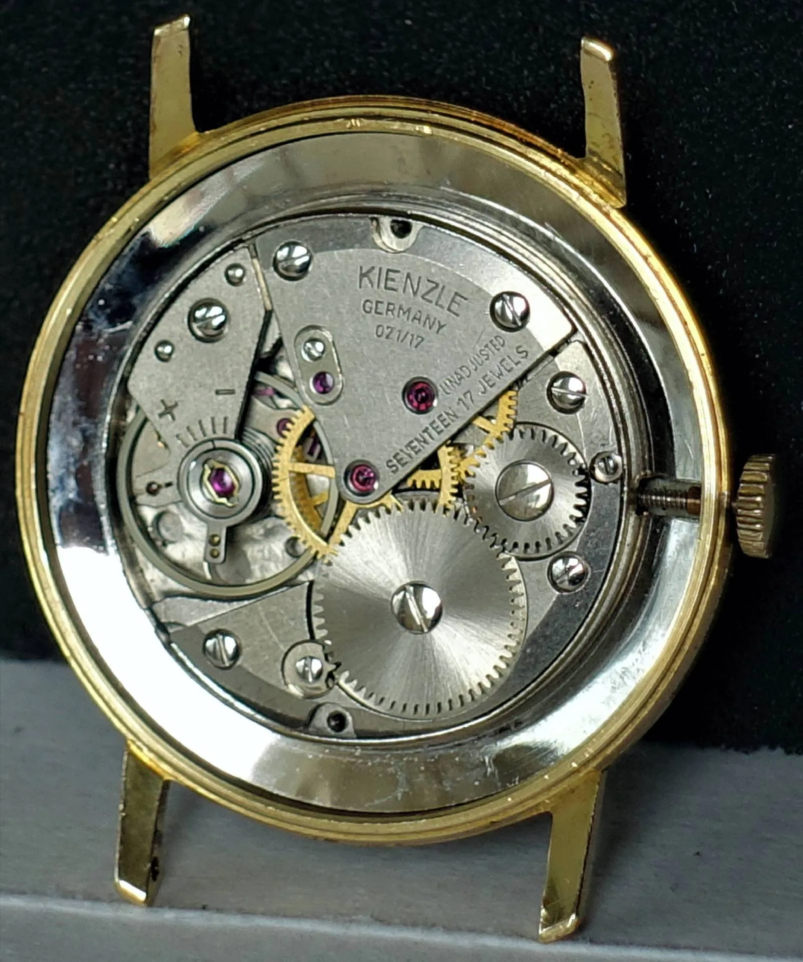Mechanisches Uhrwerk von Kienzle in einem goldfarbenen Gehäuse, sichtbare Zahnräder und Schrauben.