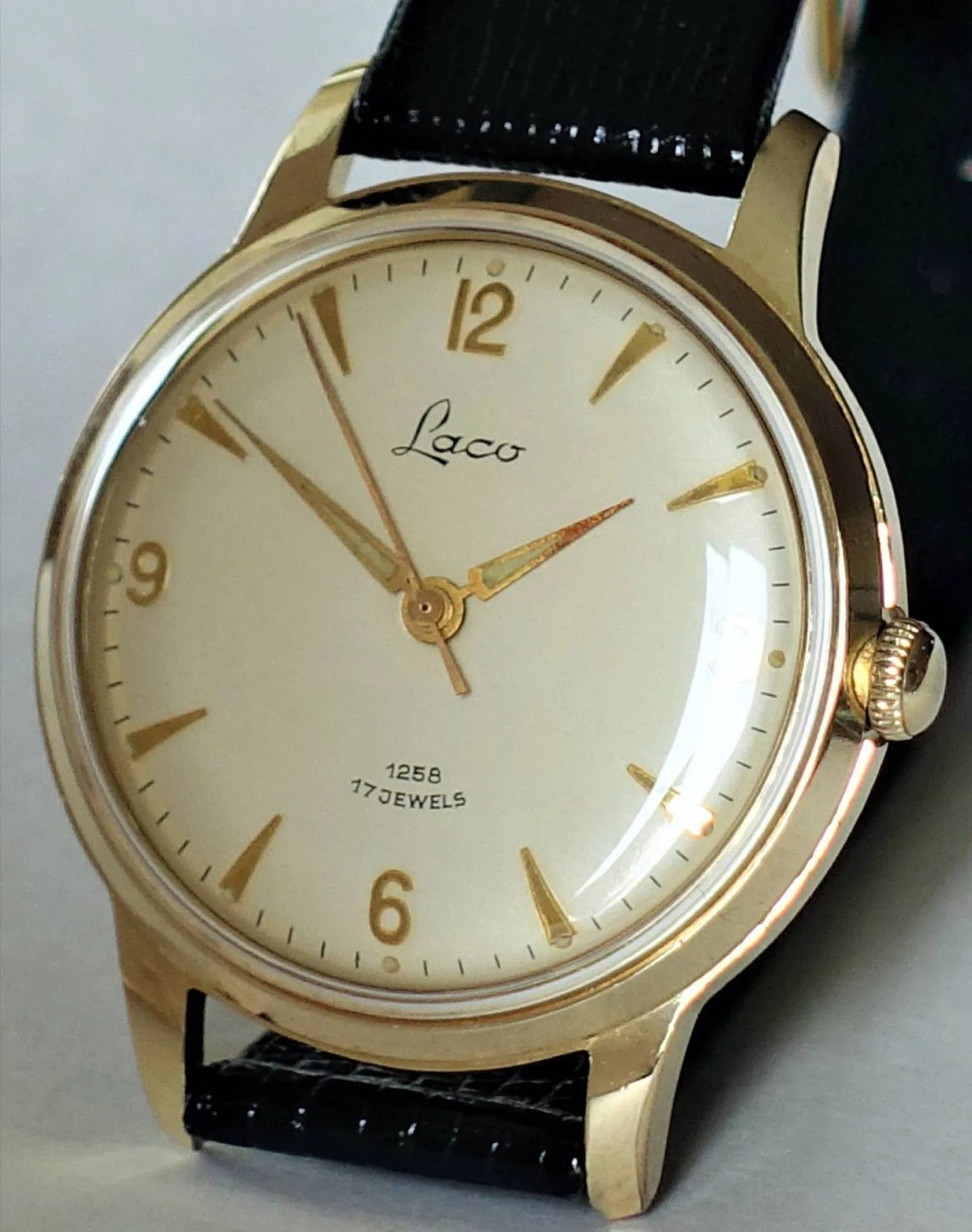Goldfarbene Armbanduhr mit hellem Zifferblatt, goldenen Indizes und schwarzem Armband.