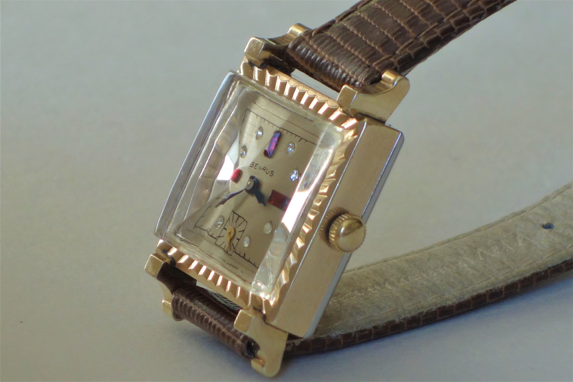 Rechteckige Armbanduhr mit goldfarbenem Gehäuse und braunem Lederarmband.