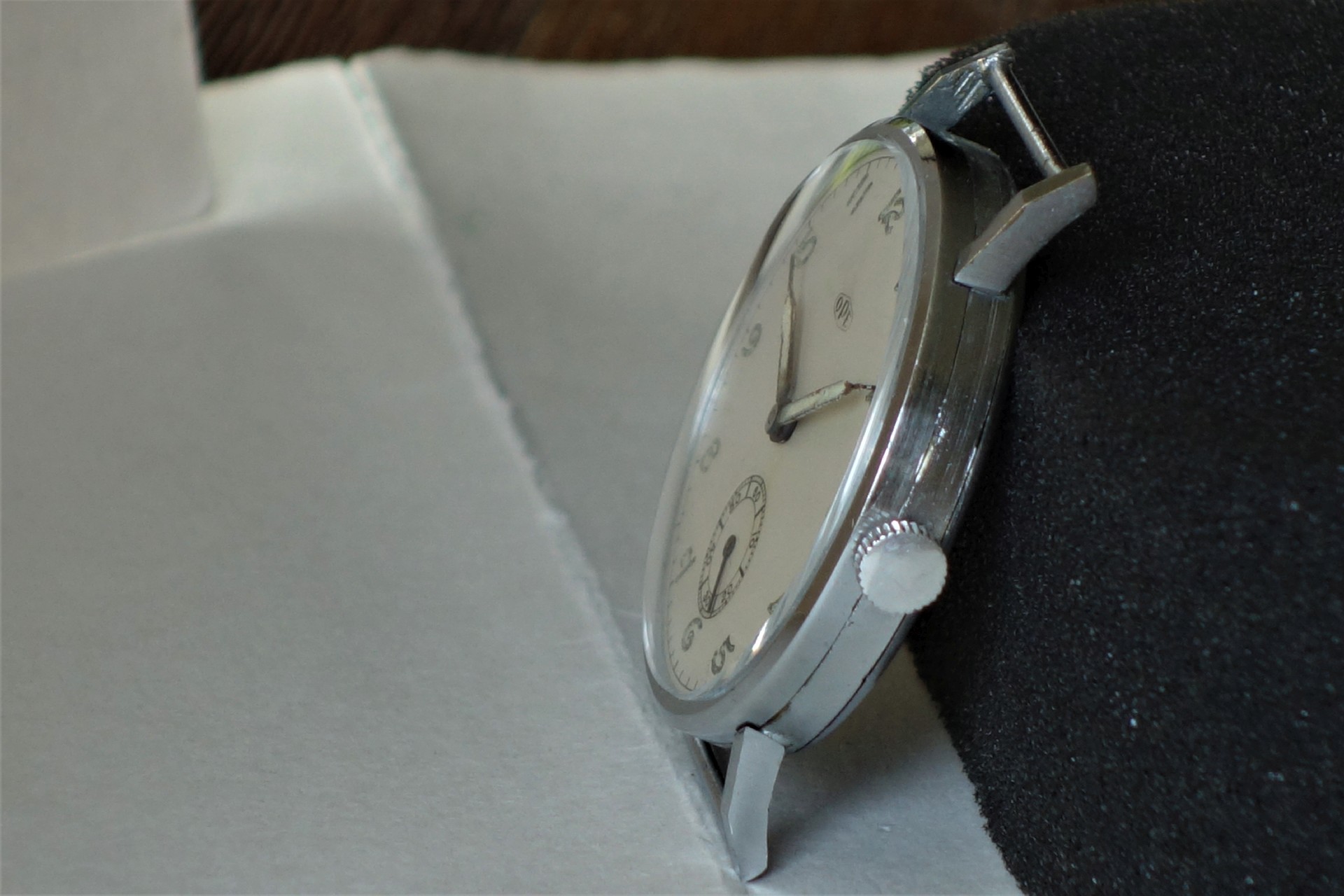 Flache analoge Armbanduhr mit silberfarbenem Gehäuse und weißem Zifferblatt.