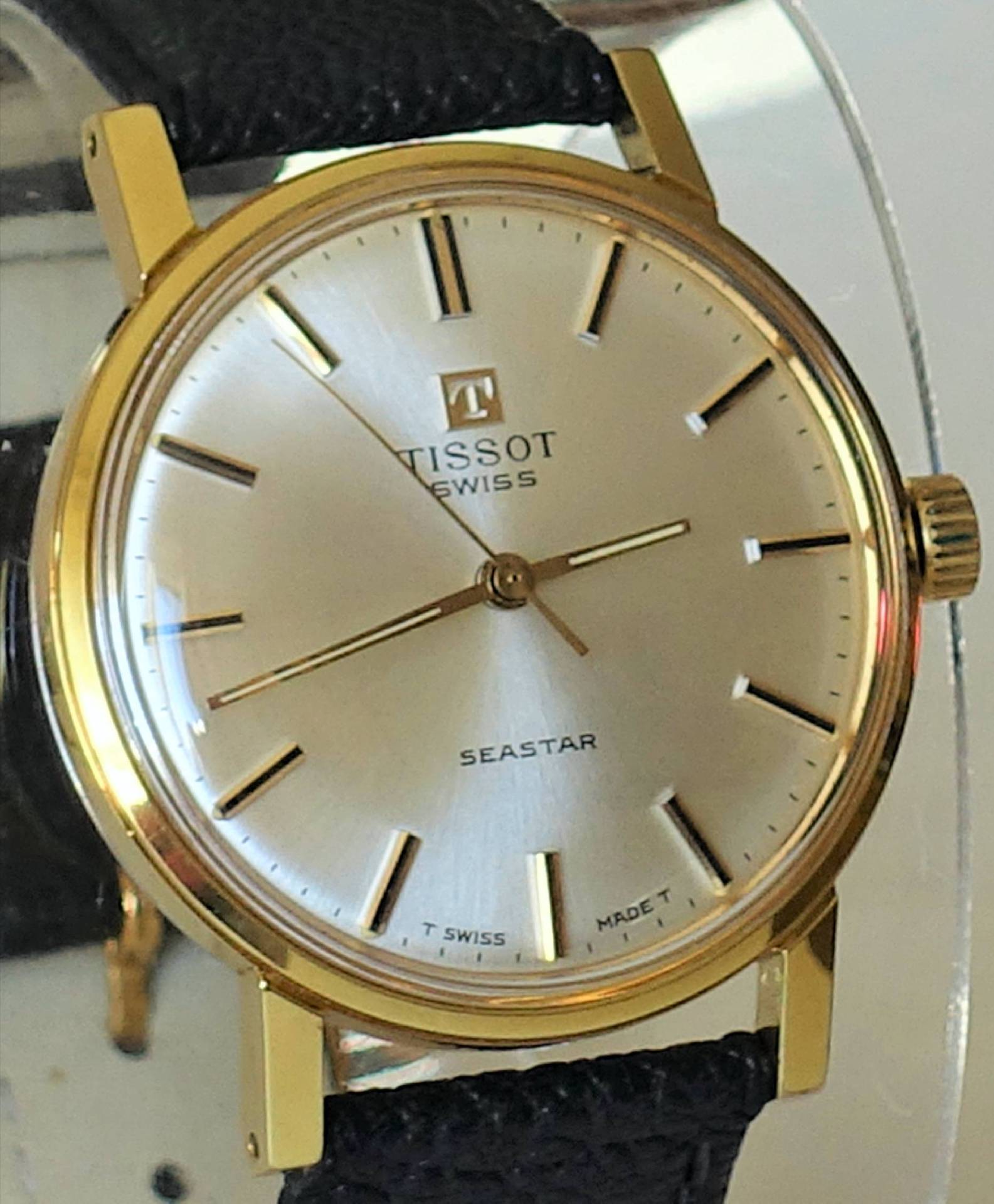 Klassische Armbanduhr mit goldfarbenem Gehäuse, silberfarbenem Zifferblatt und schwarzem Armband.