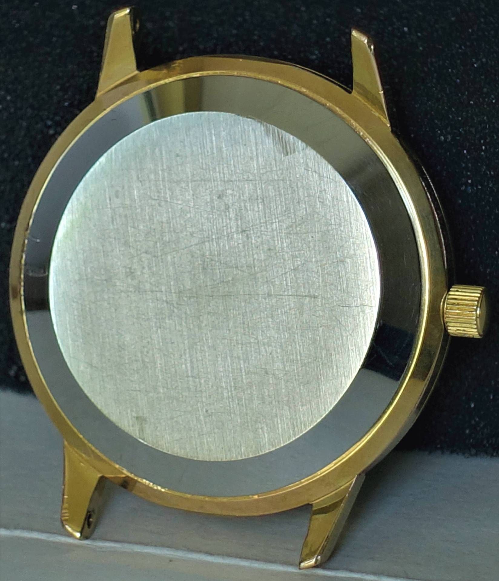 Rundes Uhrengehäuse in goldfarbener Optik mit silberfarbener Rückseite und seitlicher Krone.