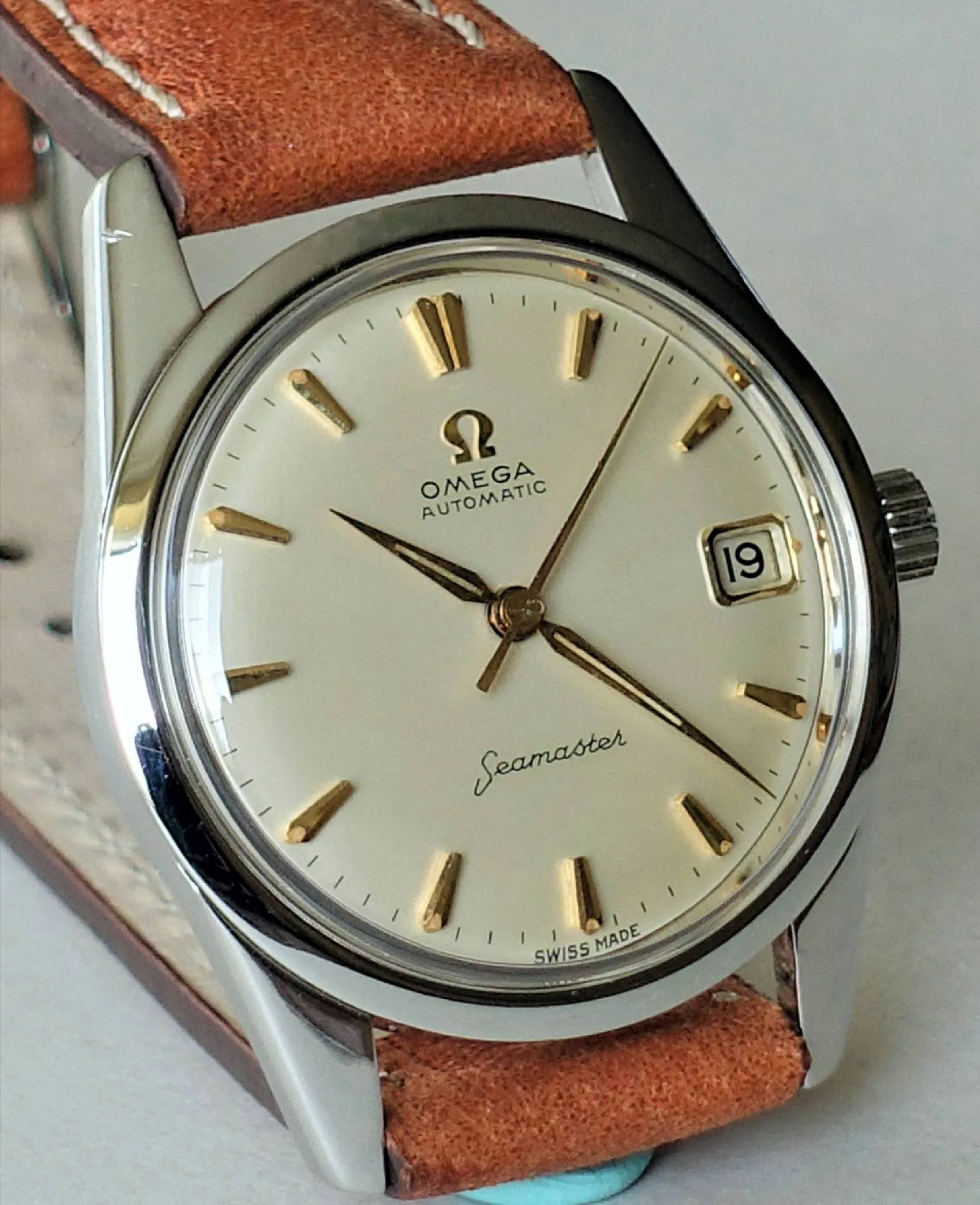 Omega Seamaster Armbanduhr Silberfarbene Armbanduhr mit beigem Zifferblatt, goldfarbenen Indizes und braunem Lederarmband.