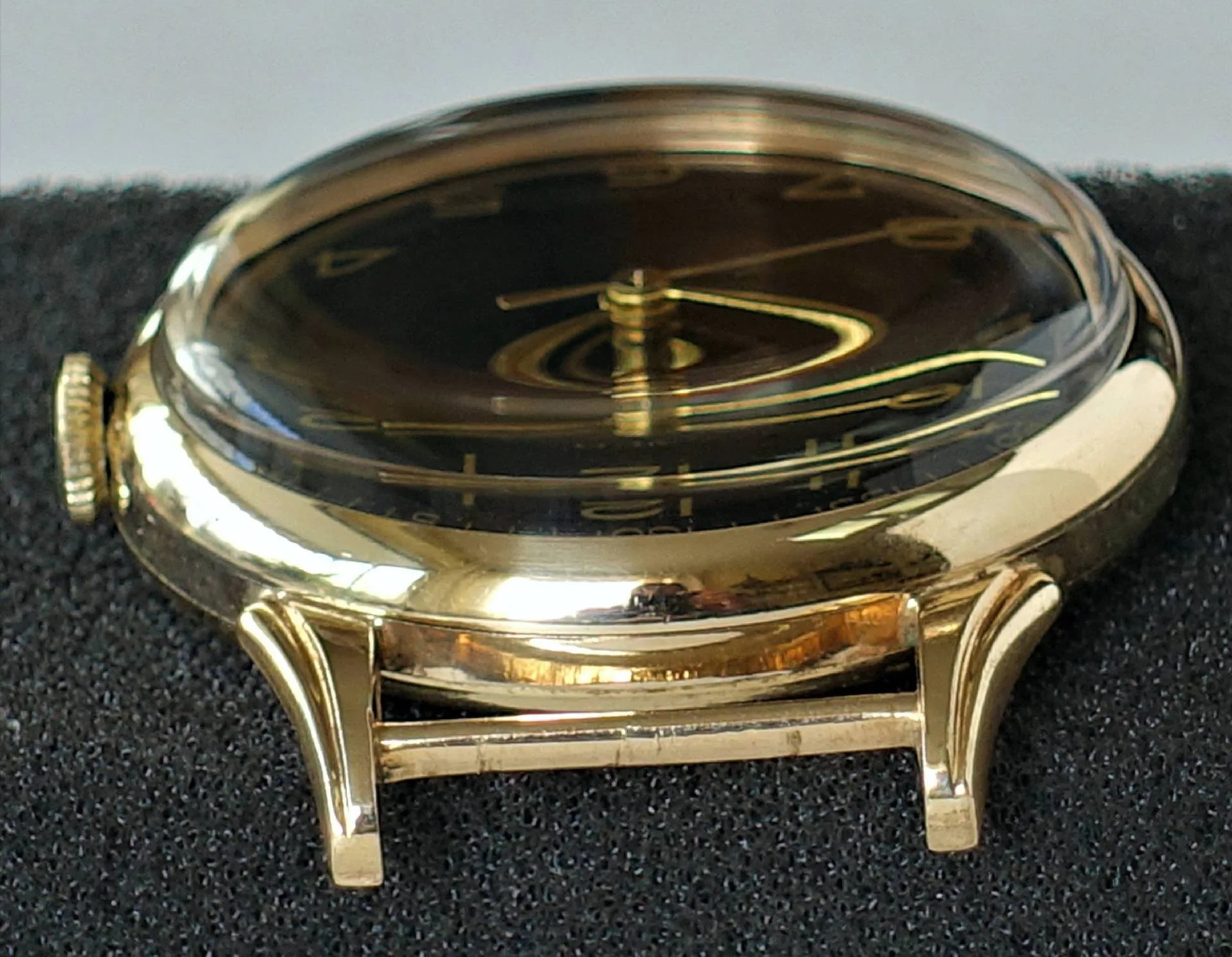 Eine Armbanduhr mit gelbglänzendem Gehäuse und schwarzem Zifferblatt liegt seitlich auf schwarzem Stoff.