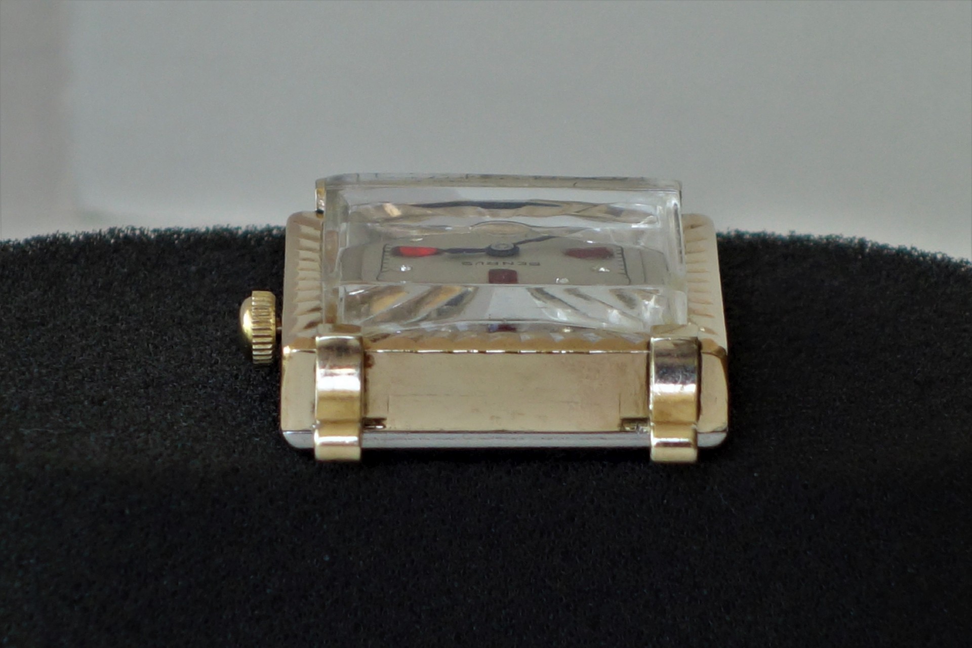 Rechteckige Armbanduhr mit goldfarbenem Gehäuse und markantem, facettiertem Kunststoffglas.