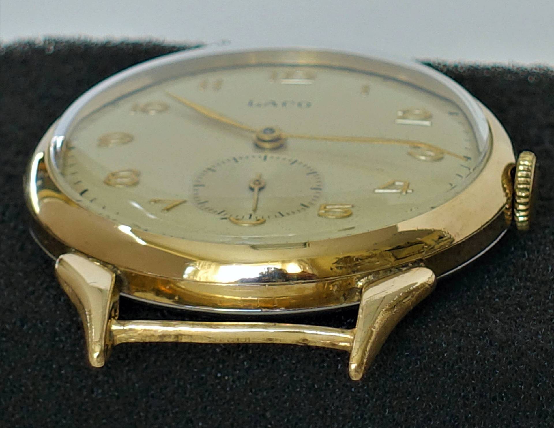 Flache Armbanduhr mit goldfarbenem Gehäuse und hellem Zifferblatt.