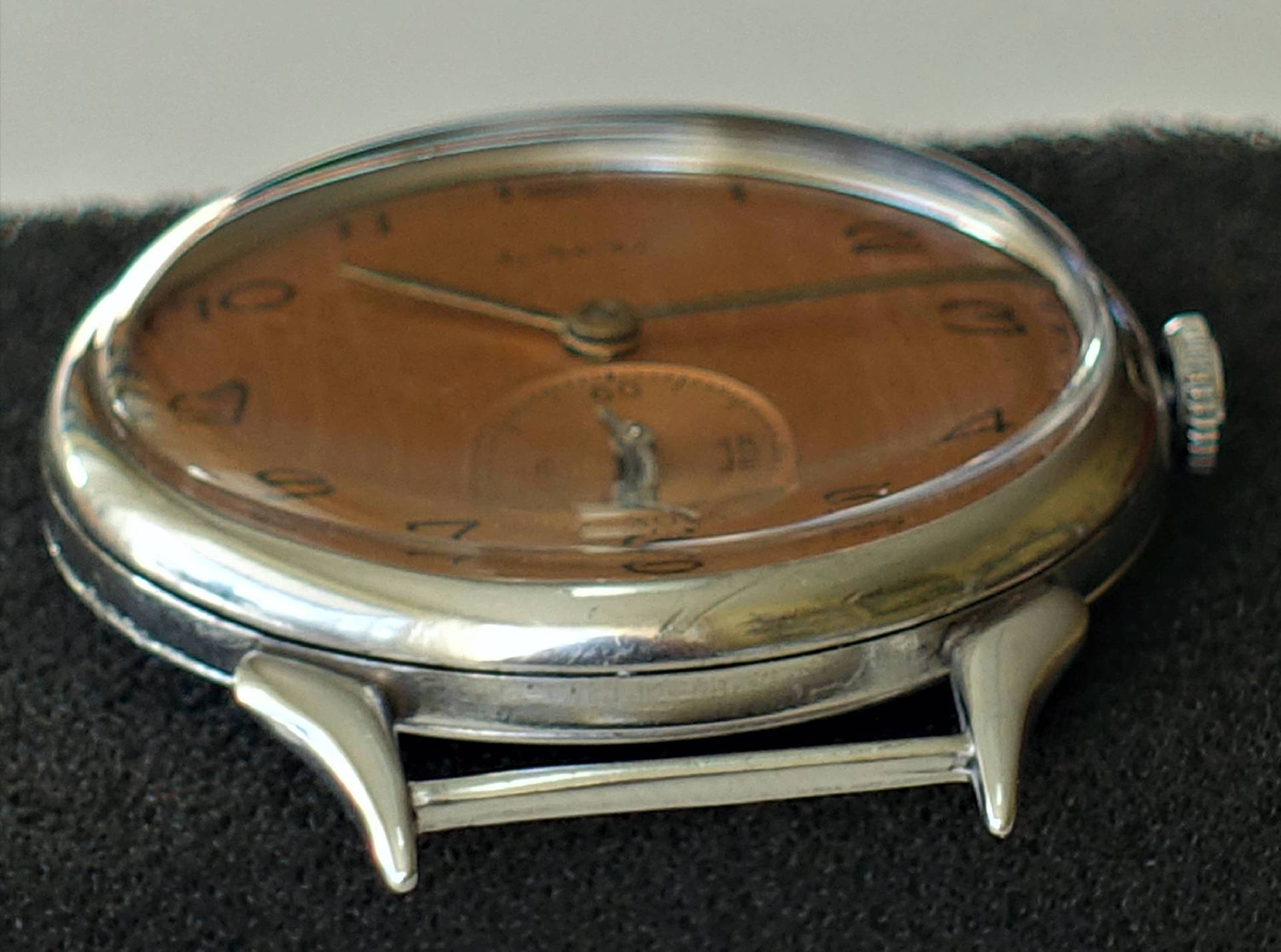 Silberfarbene Armbanduhr mit braunem Zifferblatt und schwarzer Beschriftung.