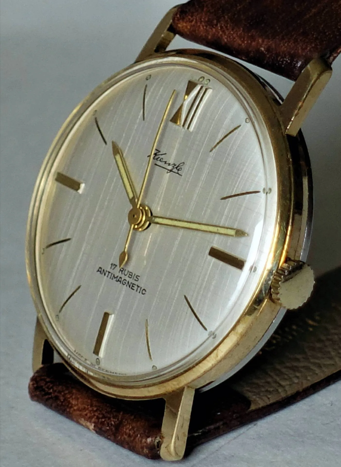 Goldfarbene Armbanduhr mit hellem Zifferblatt und braunem Armband.