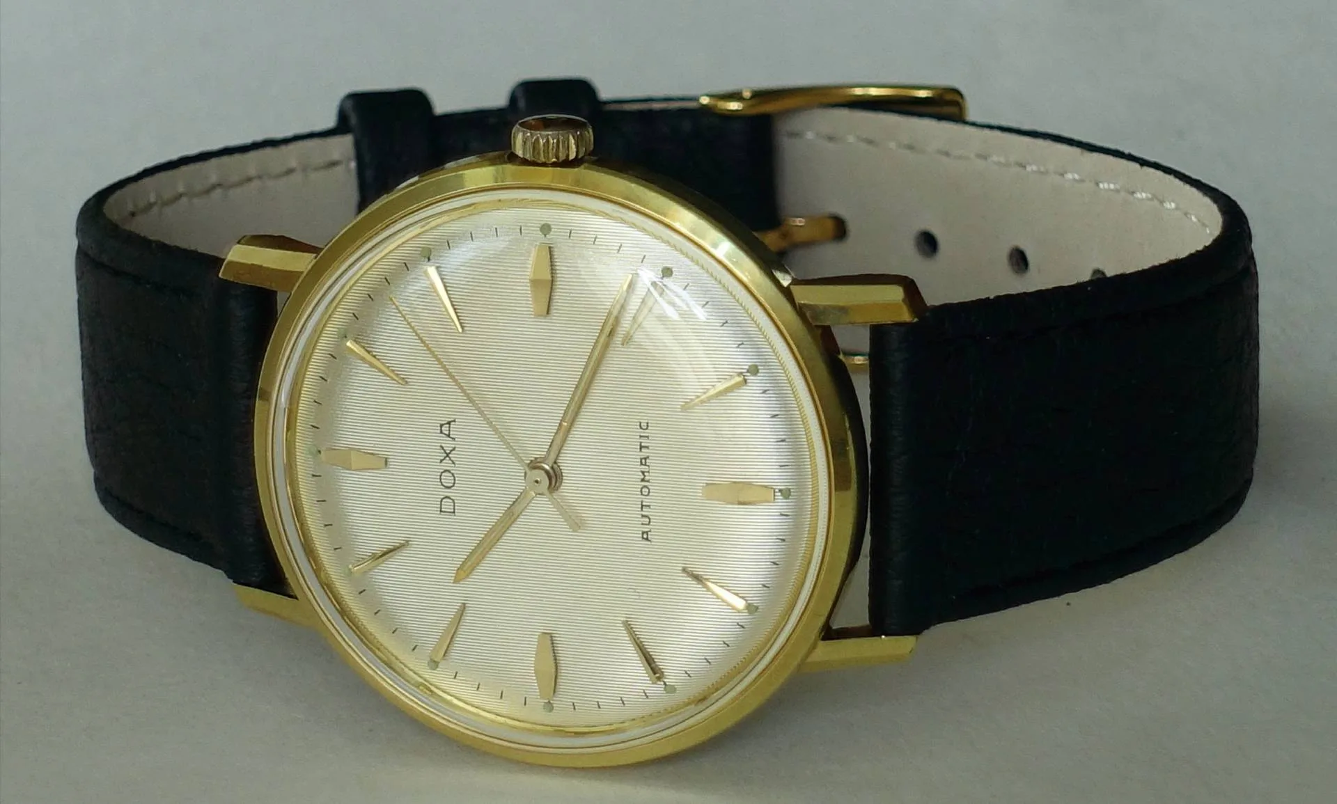 Goldfarbene Armbanduhr mit hellem Zifferblatt und schwarzem Armband.