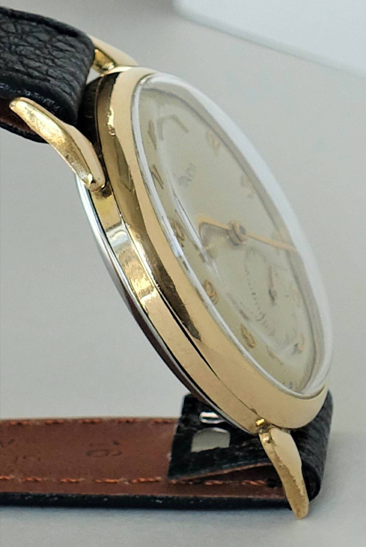 Goldfarbene Armbanduhr mit schwarzem Lederarmband und hellem Zifferblatt.