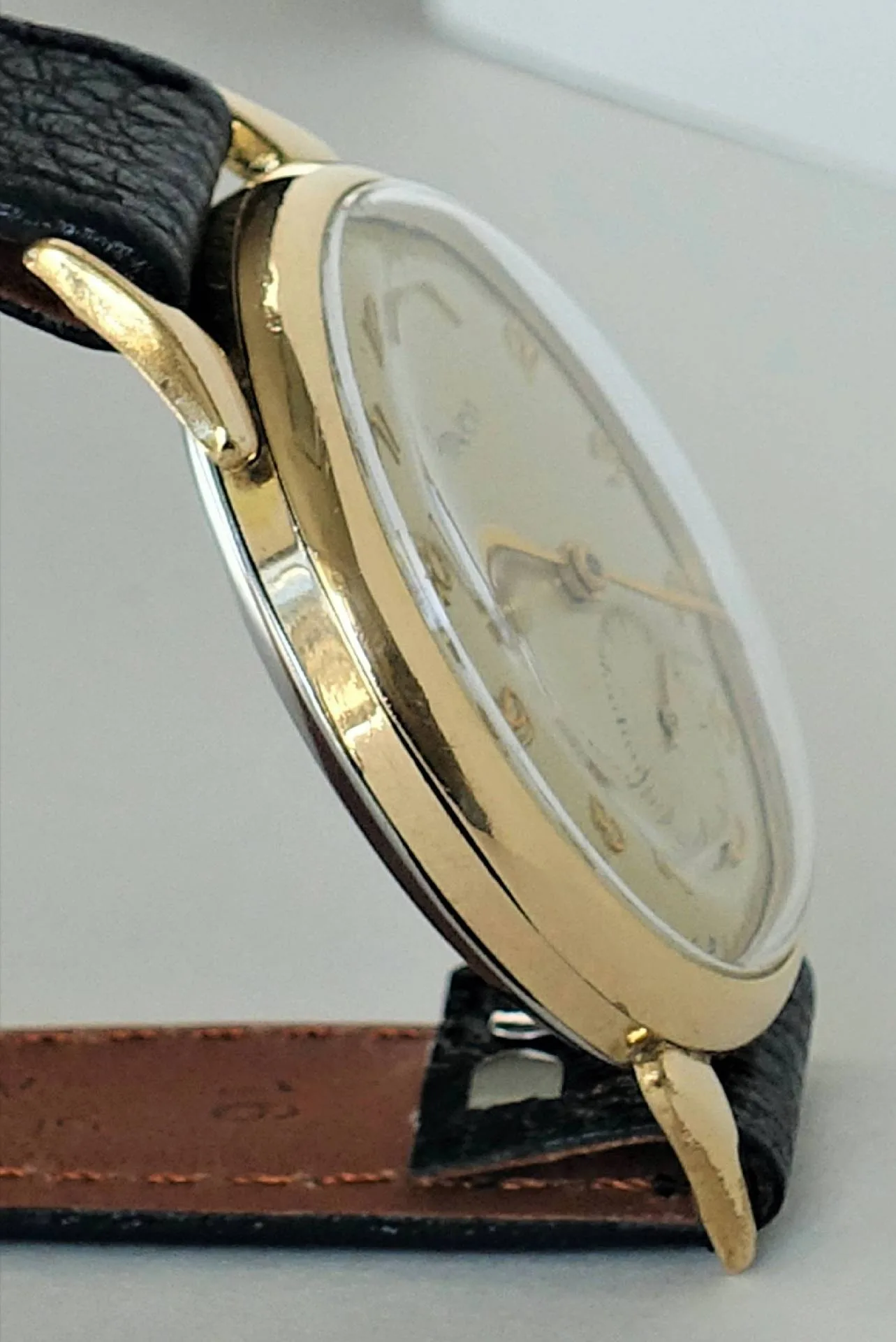 Armbanduhr goldfarben Goldfarbene Armbanduhr mit schwarzem Lederarmband und hellem Zifferblatt.