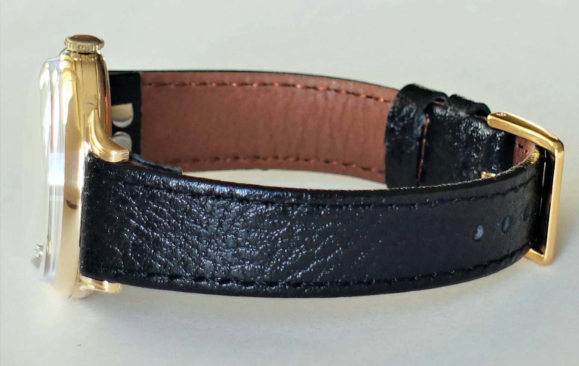 Schwarzes Lederband, gelbfarbenes Gehäuse, klassische Uhr Eine Armbanduhr mit schwarzem Lederarmband und gelbfarbenem Gehäuse liegt seitlich auf einer hellen Oberfläche.