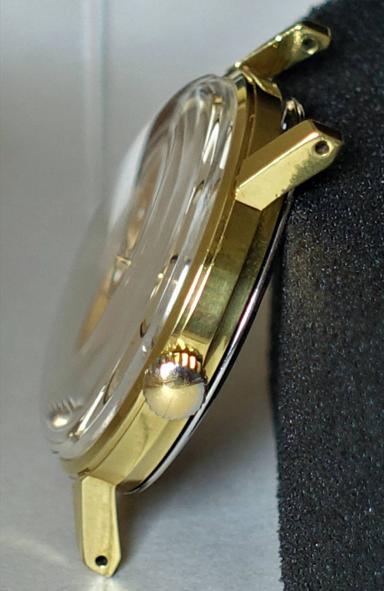 Goldfarbenes Uhrengehäuse mit transparenter Abdeckung und seitlicher Krone.