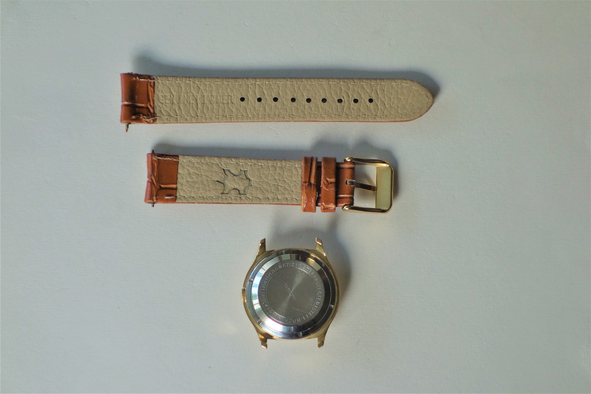 Zerlegtes Uhrgehäuse in goldfarben mit beigem und braunem Lederarmband und goldfarbener Schließe.