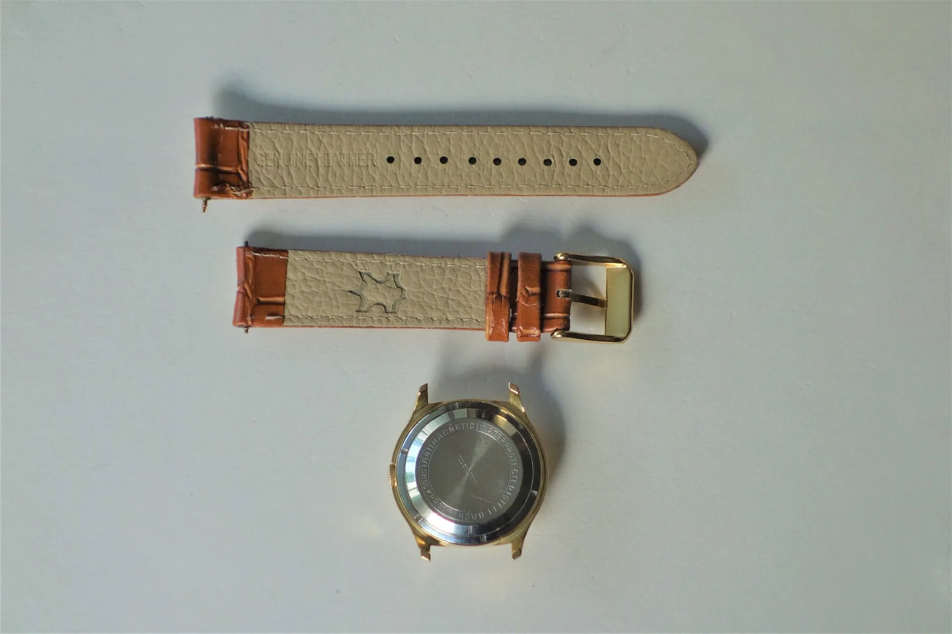 Uhrgehäuse mit Lederarmband Zerlegtes Uhrgehäuse in goldfarben mit beigem und braunem Lederarmband und goldfarbener Schließe.