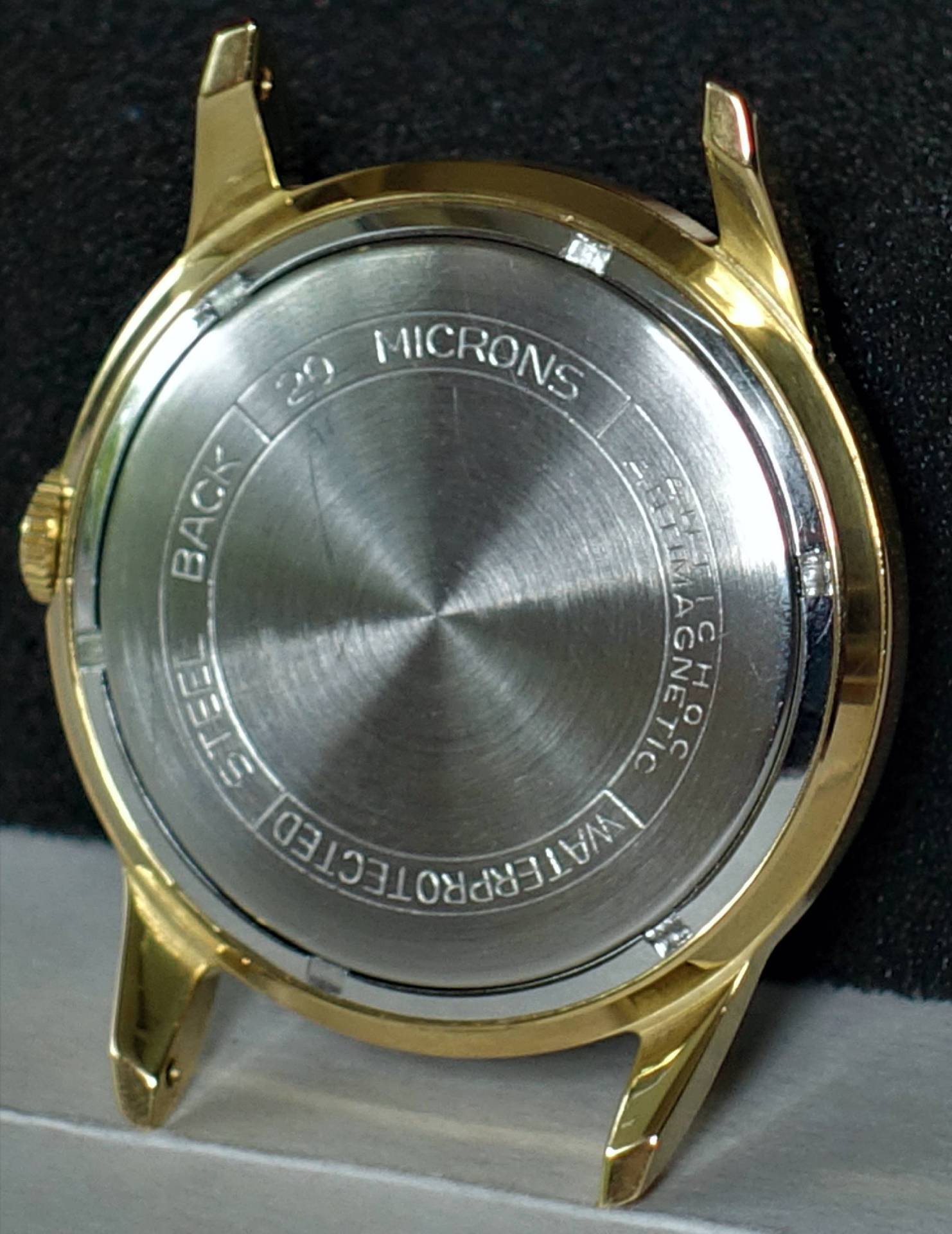 Rundes goldfarbenes Uhrgehäuse mit silberfarbener Rückseite.