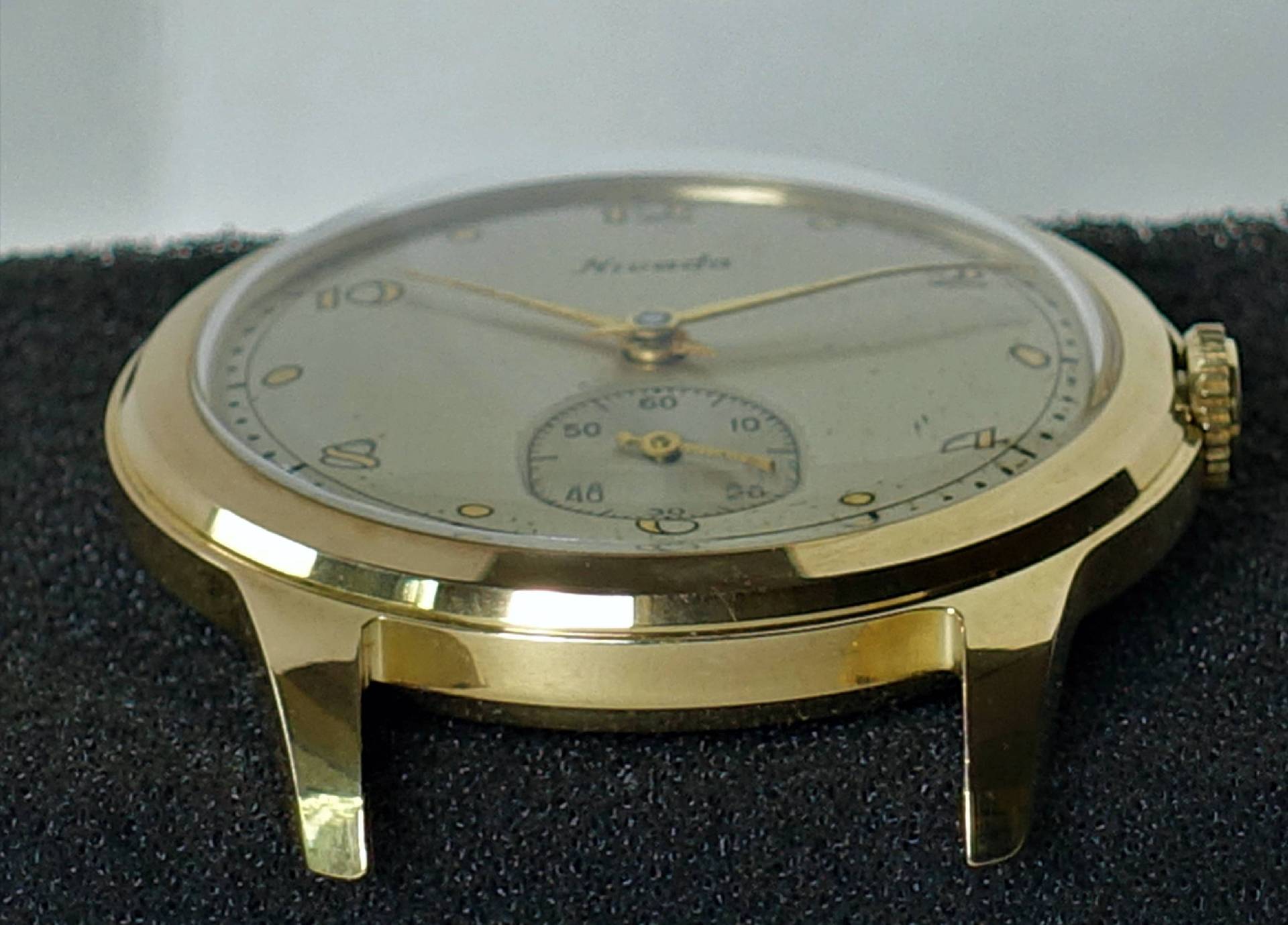 Flache Armbanduhr mit goldfarbenem Gehäuse und hellem Zifferblatt.