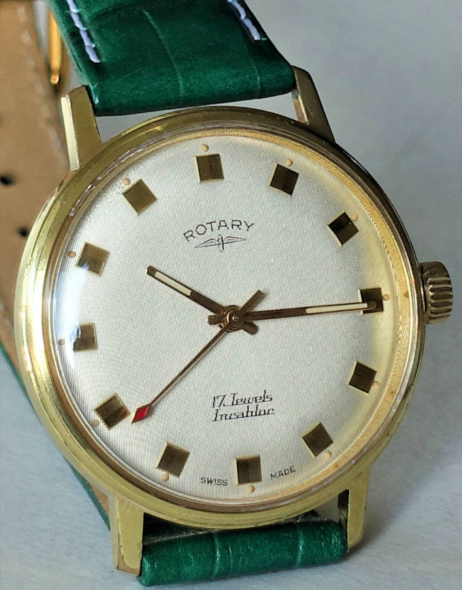 Goldfarbene Armbanduhr mit weißem Zifferblatt und grünem Armband.