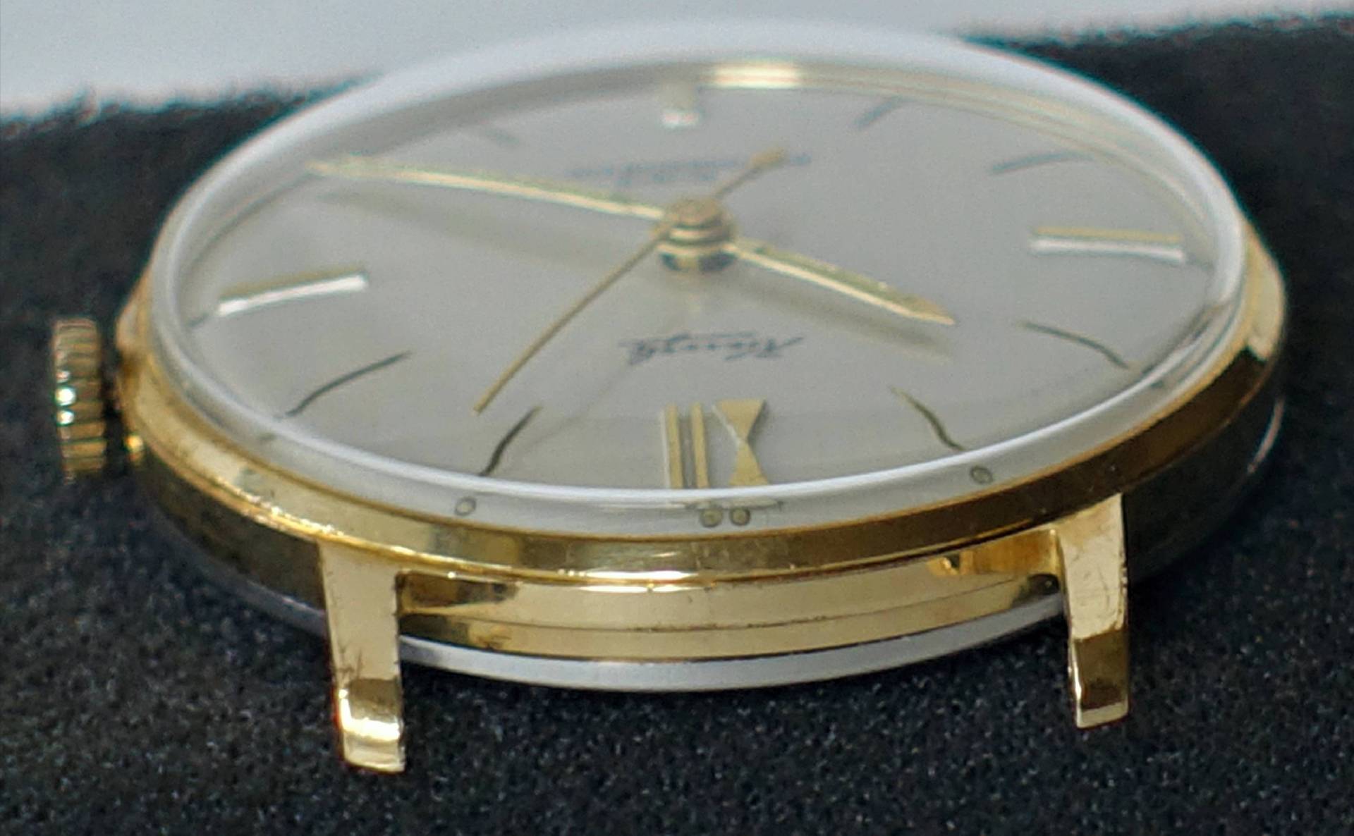 Flache Armbanduhr mit goldfarbenem Gehäuse und hellem Zifferblatt.