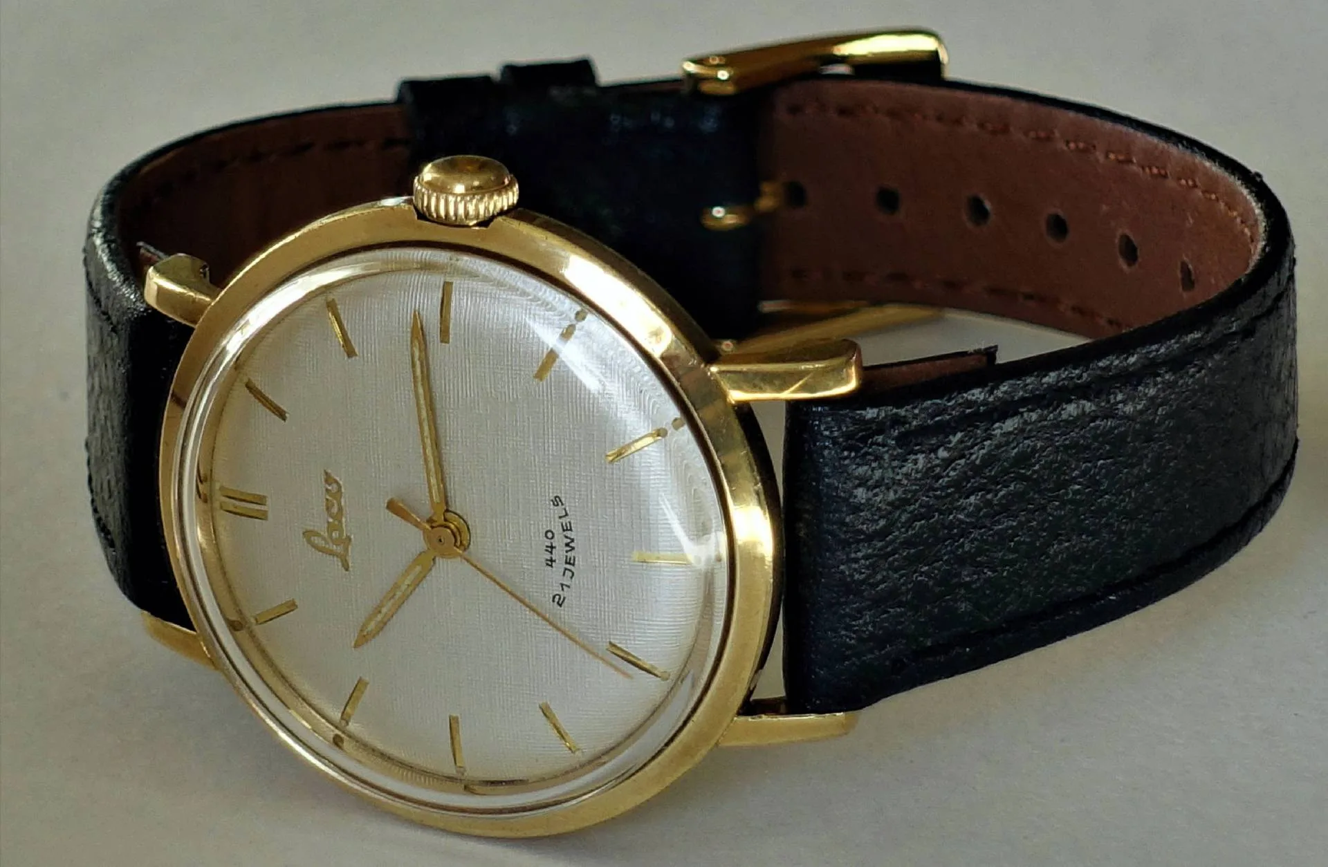 Analoge Armbanduhr mit goldfarbenem Gehäuse, weißem Zifferblatt und schwarzem Armband.