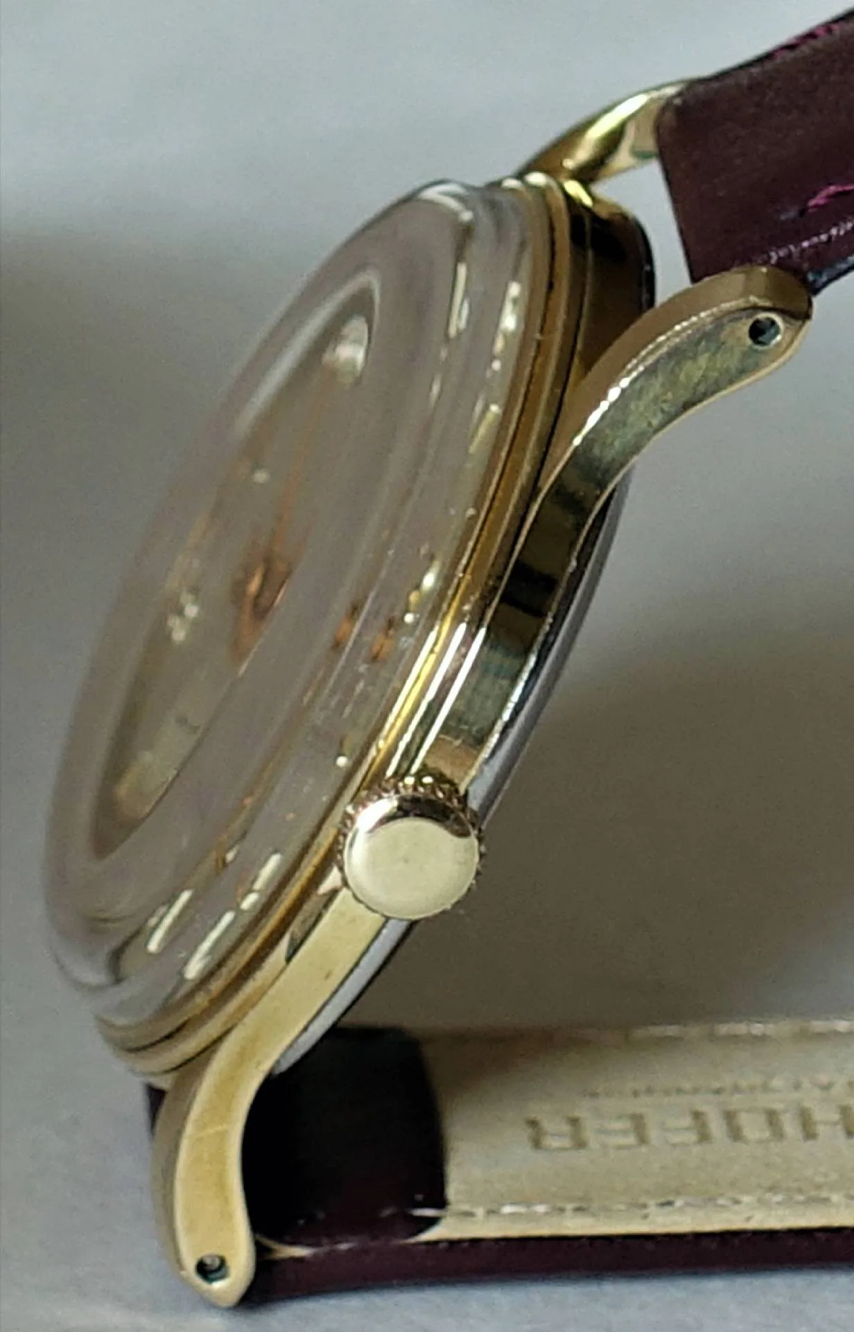 Uhrgehäuse goldfarben Seitliche Ansicht eines goldfarbenen Uhrgehäuses mit Krone und braunem Lederarmband.