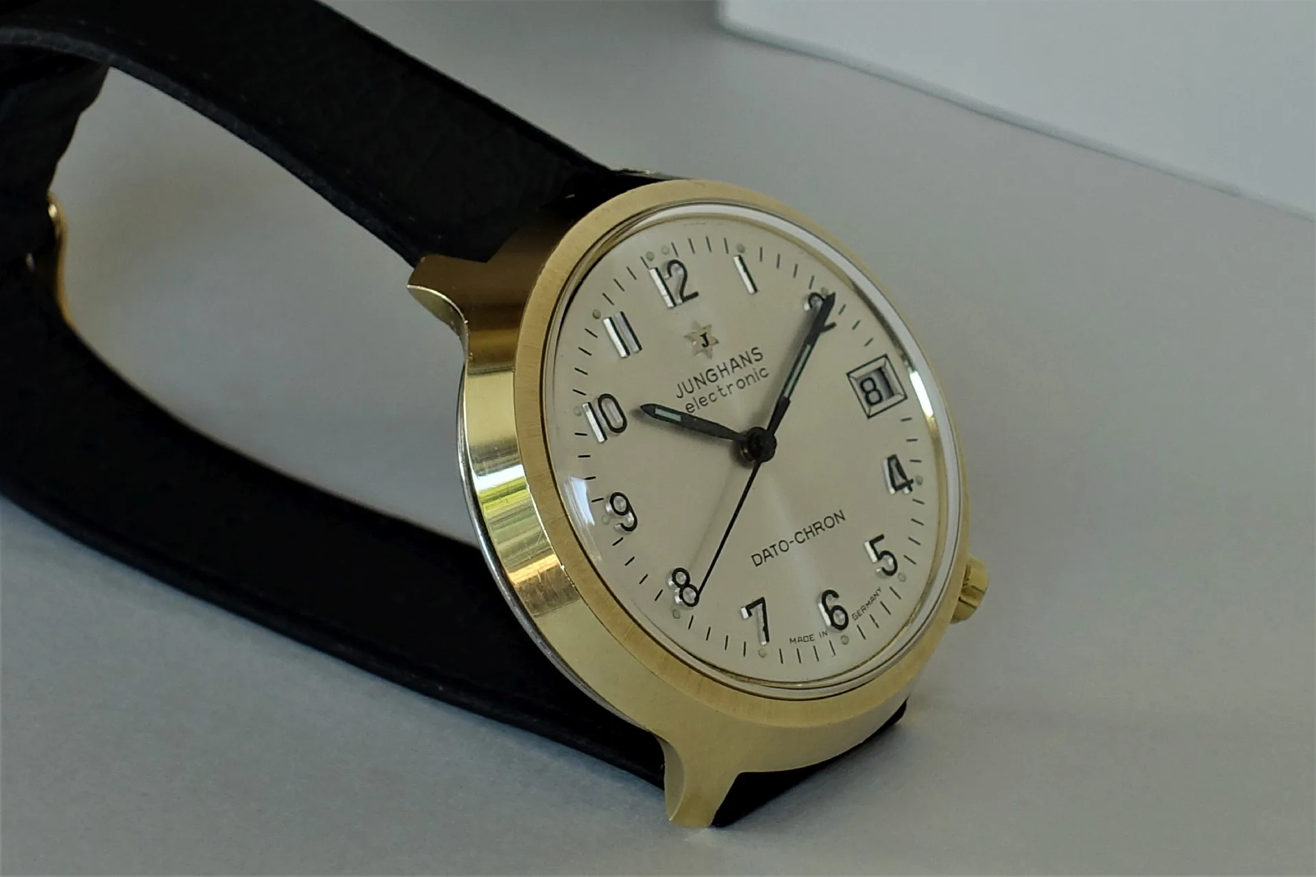Junghans Armbanduhr goldfarben Analoge Armbanduhr mit goldfarbenem Gehäuse, hellem Zifferblatt und schwarzem Armband.