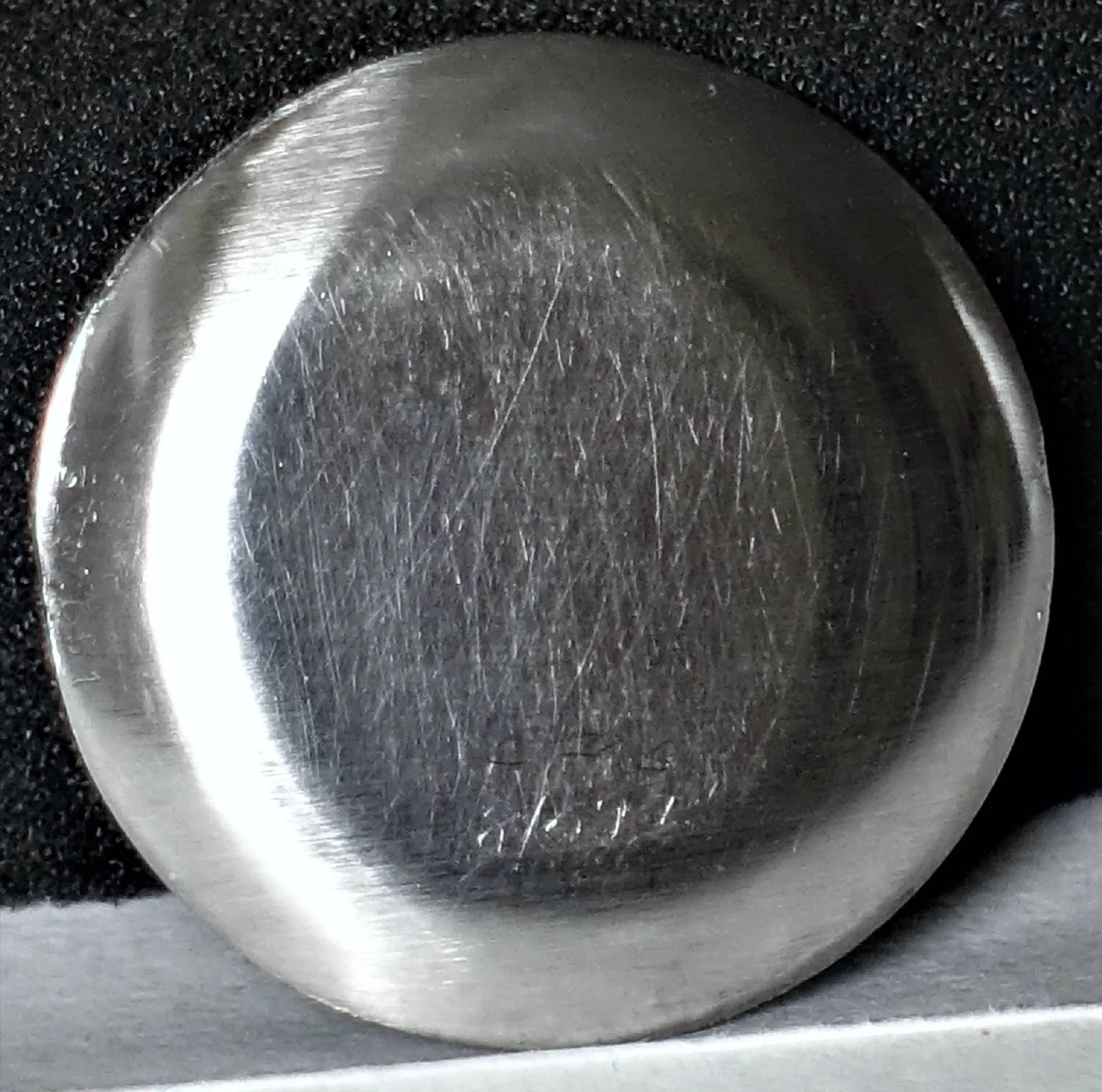 Silberfarbener Uhrendeckel Rückseite Eine silberfarbene, runde Rückseite eines Uhrendeckels mit sichtbaren feinen Kratzern liegt auf schwarzem Untergrund.