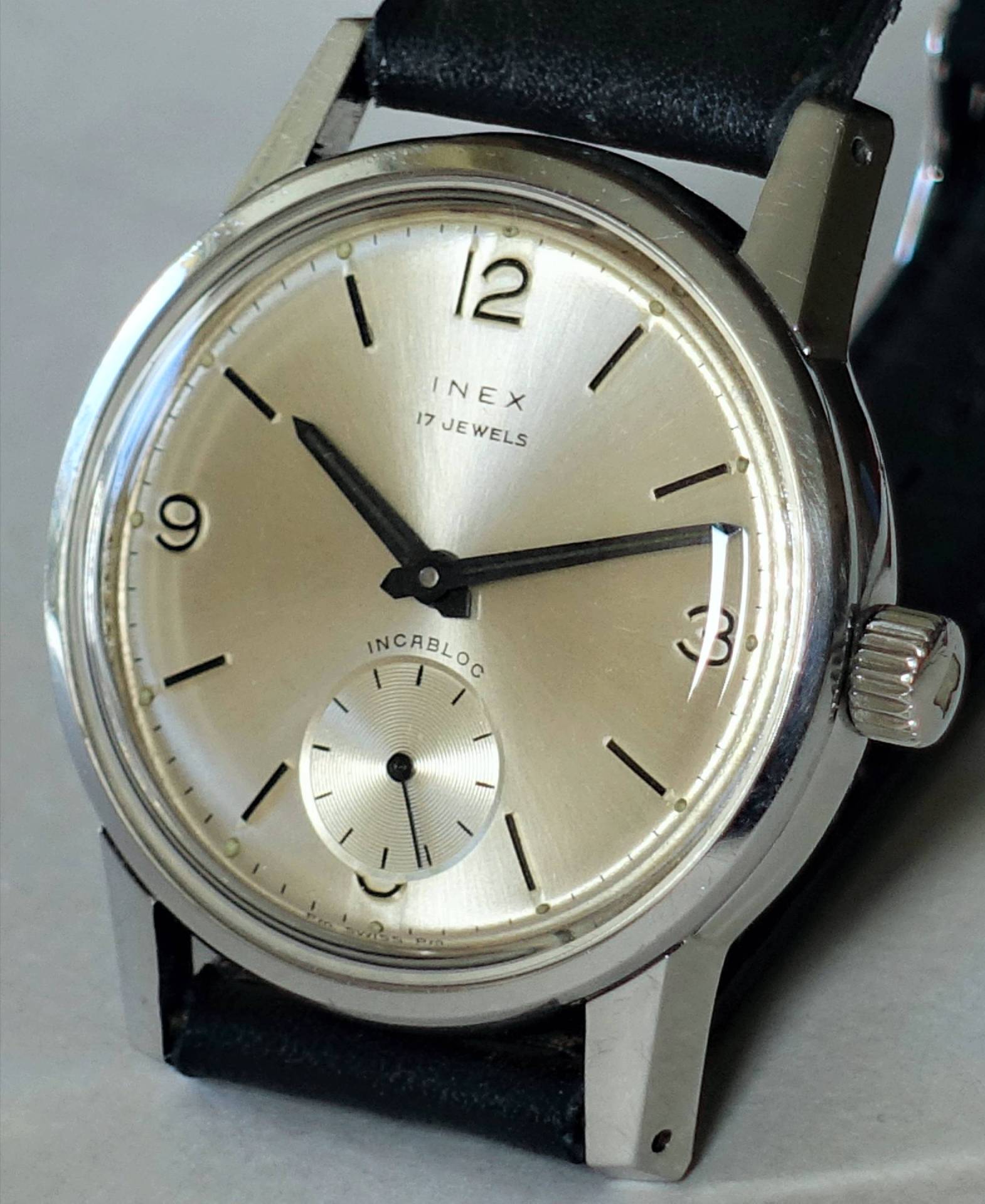 Detailaufnahme einer INEX Armbanduhr mit silbernem Ziffernblatt und schwarzem Lederarmband