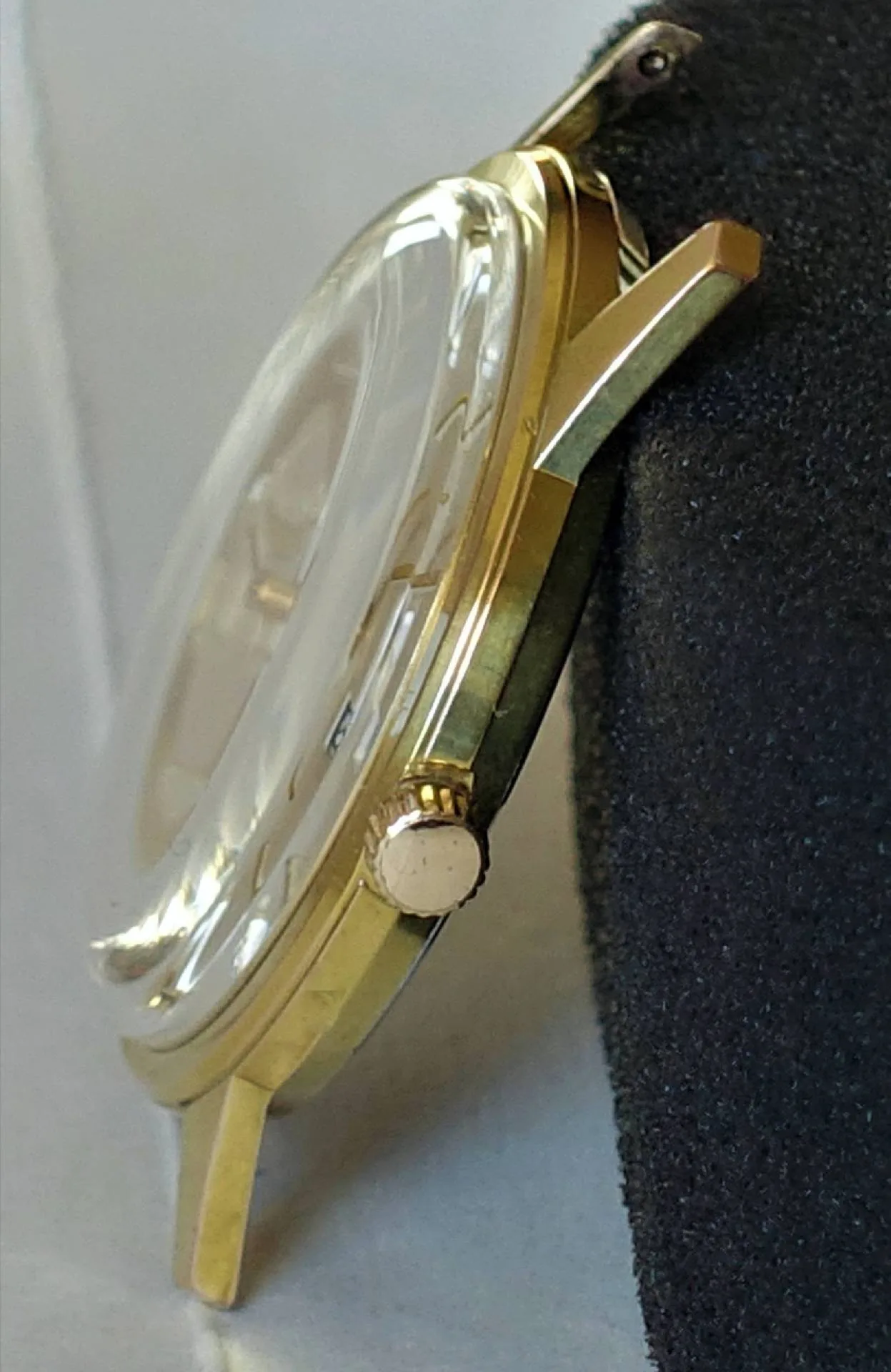 Flaches Gehäuse, goldfarbene Uhr Seitliche Nahaufnahme einer flachen Armbanduhr mit goldfarbenem Gehäuse, gewölbtem Glas und heller Krone.
