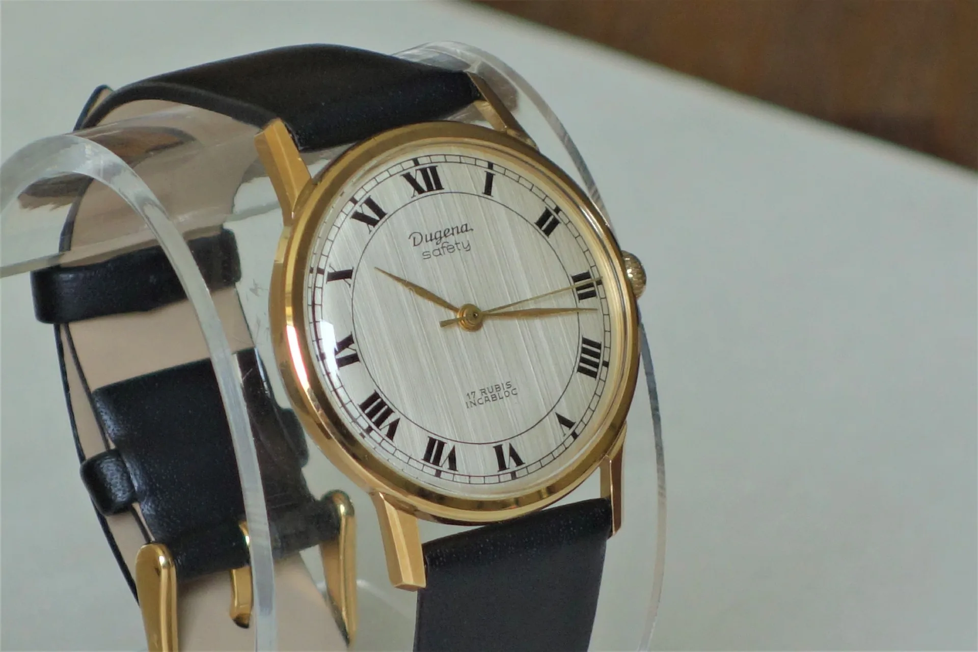 Klassische Armbanduhr mit goldfarbenem Gehäuse, weißem Zifferblatt und schwarzem Lederarmband.