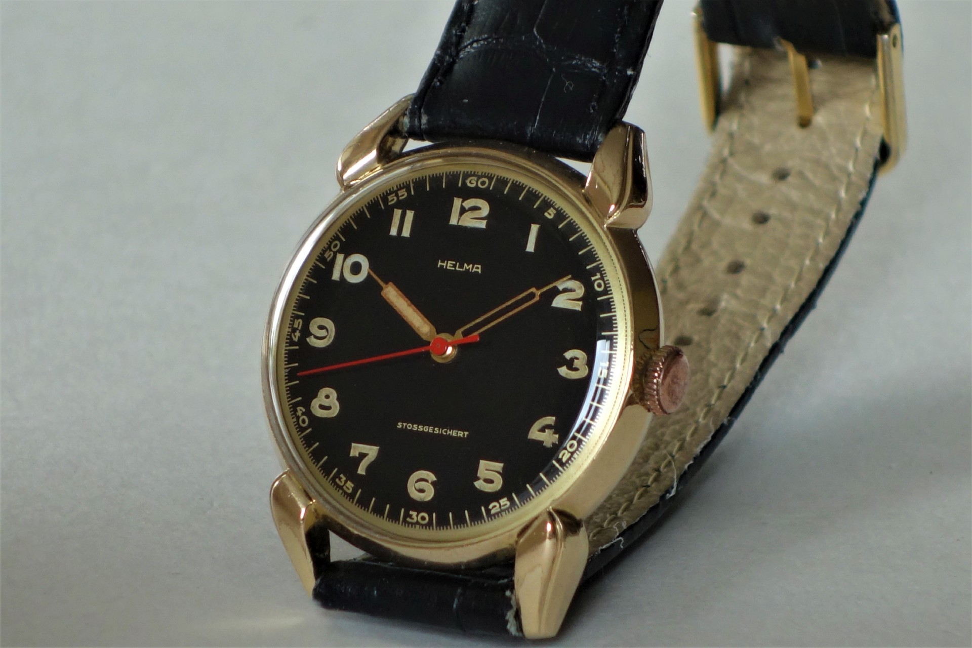 Analoge Armbanduhr mit schwarzem Zifferblatt, goldfarbenem Gehäuse und schwarzem Armband.