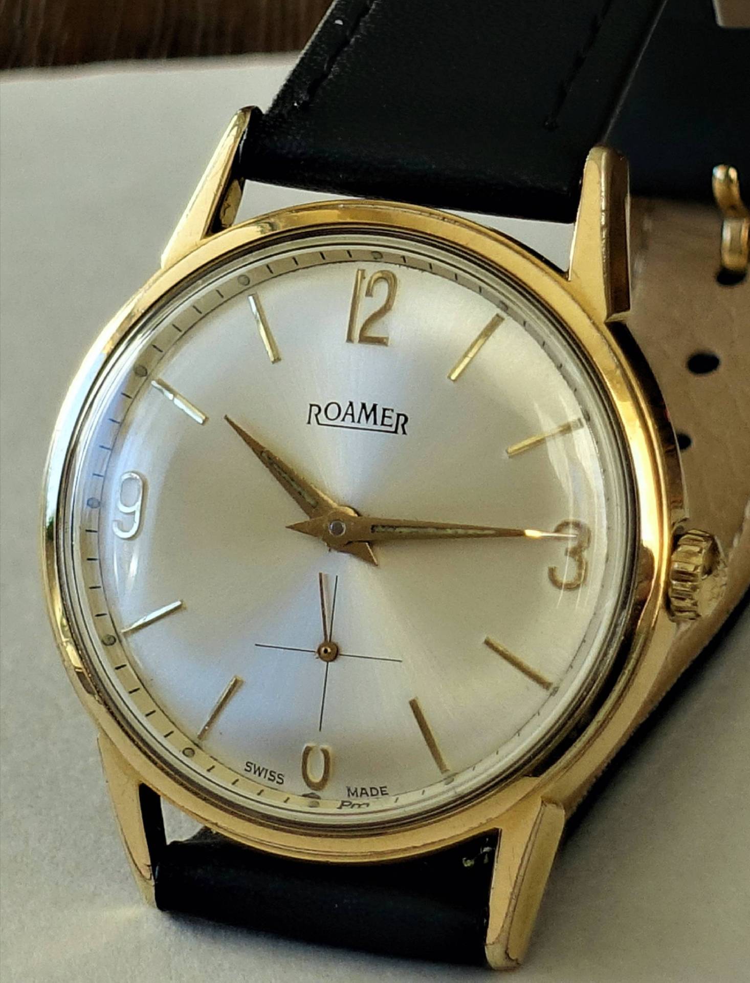 Goldfarbene Armbanduhr mit hellem Zifferblatt und schwarzem Armband.